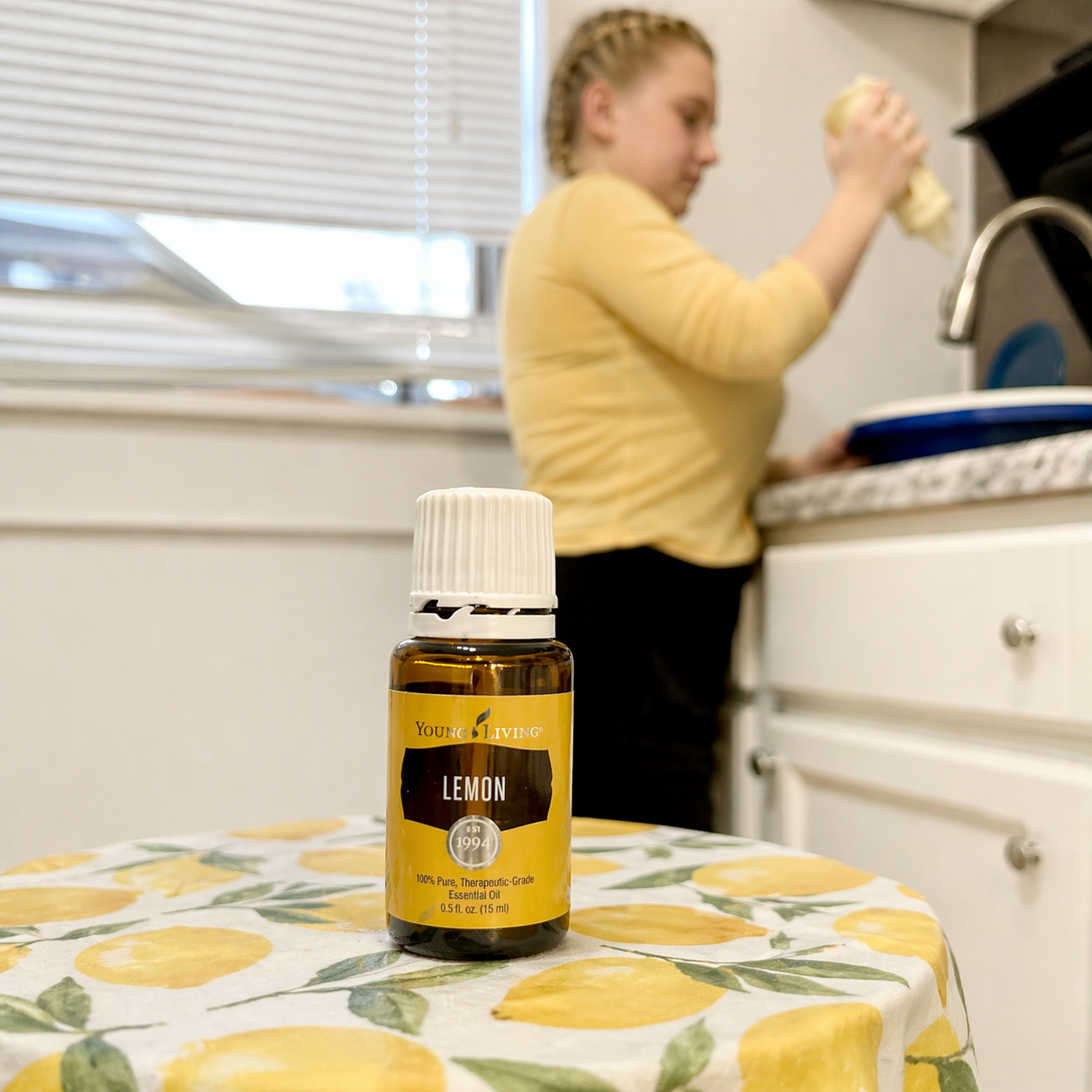 Amber medicine bottle on a lemon-patterned table, with a person washing dishes in a kitchen behind it