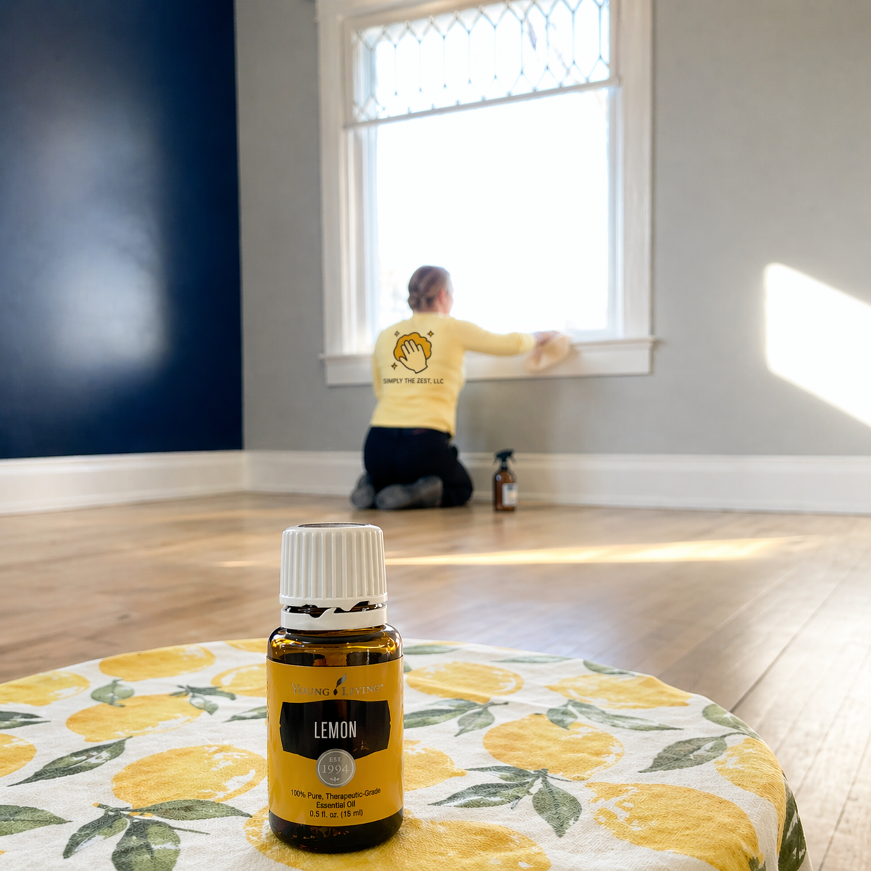 Person kneeling by a sunlit window with a diffuser bottle on a floral table in the foreground