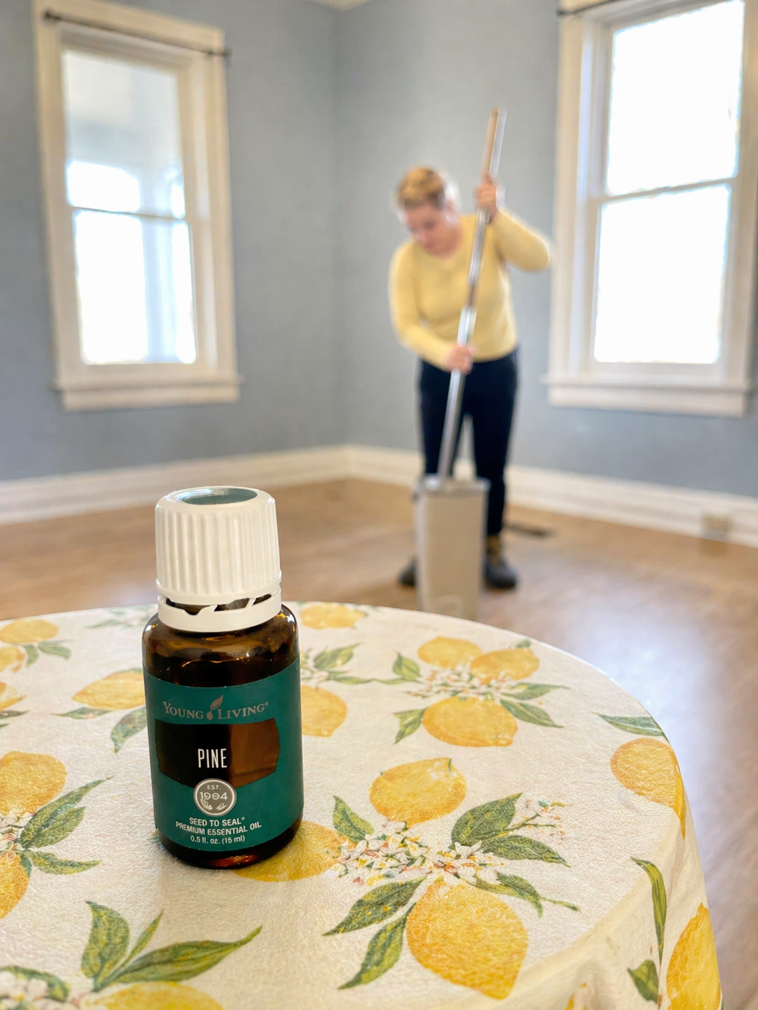 Essential oil bottle on floral tablecloth with a person vacuuming in a bright room