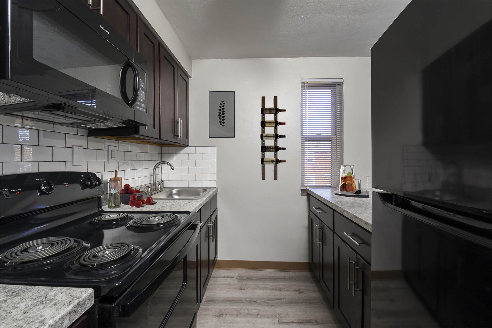 Compact modern kitchen with black appliances, white subway tile, and a wine rack at The Alden South Hills in Pittsburgh, PA.