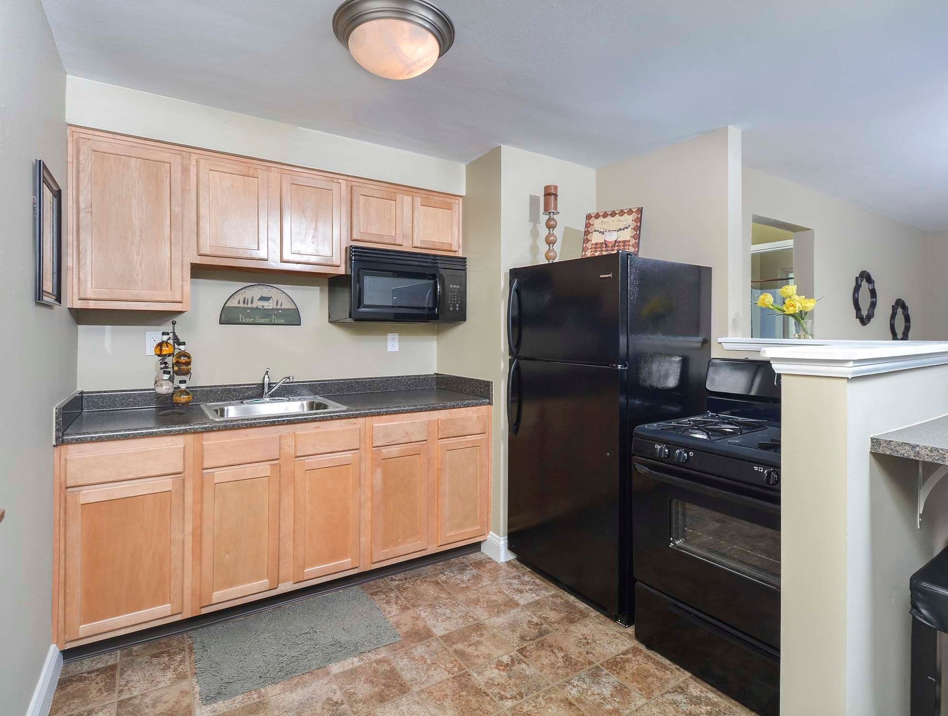 Apartment kitchen with light wood cabinets, black appliances, and dark countertops at The Alden South Hills in Pittsburgh, PA.