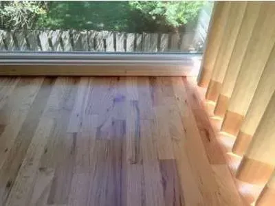 A wooden floor next to a window with blinds.