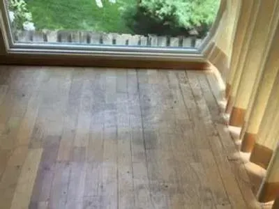 A wooden floor in a room with a window and curtains.