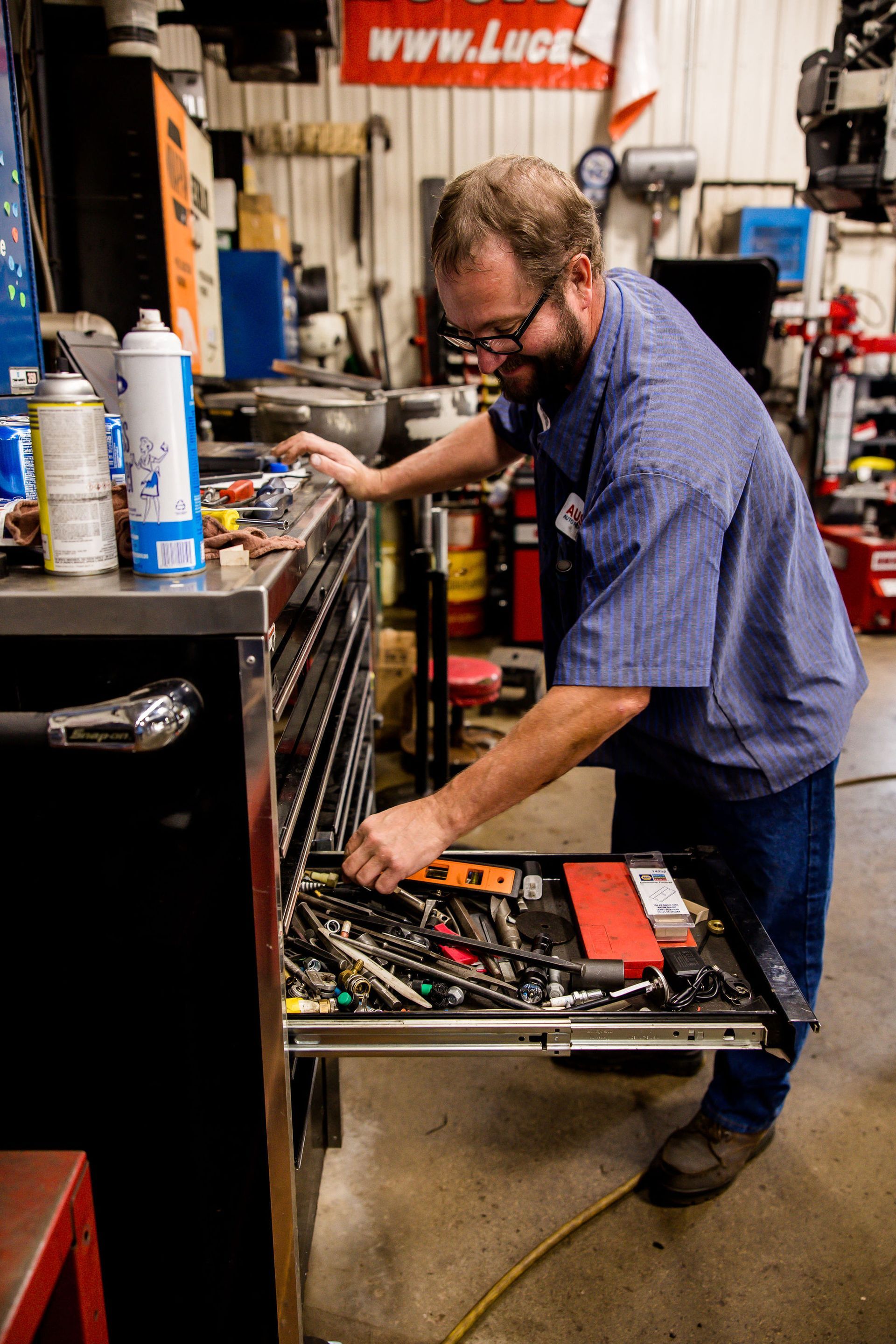 Mechanic in blue work shirt reaching into a toolbox drawer, searching for a tool in a garage.