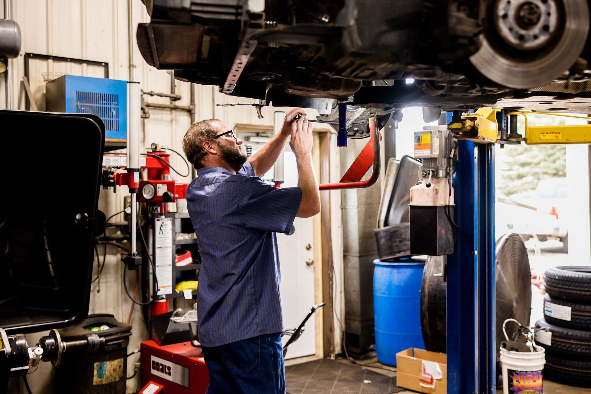 Mechanic working under a car on a lift in a repair shop.