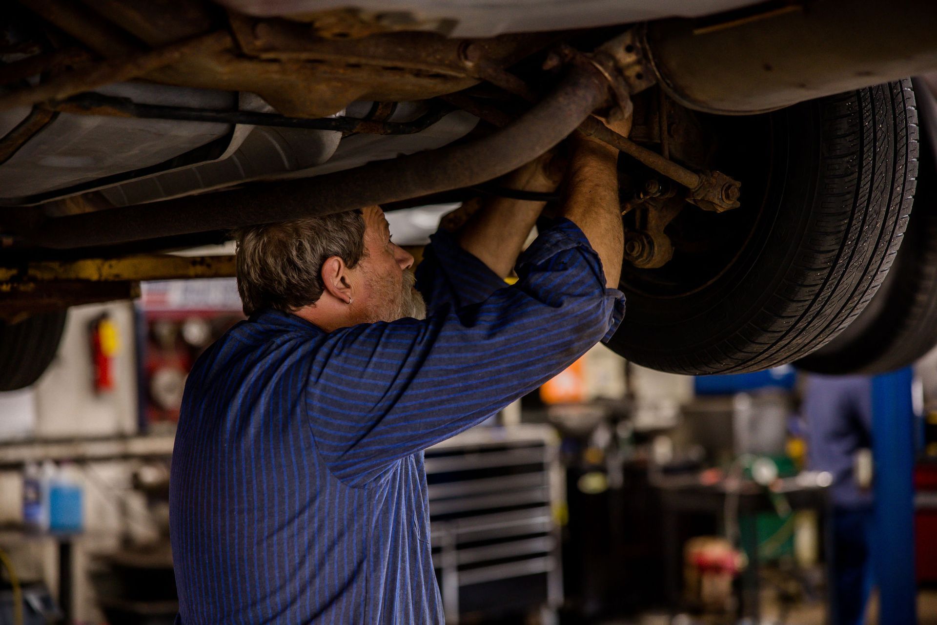 Mechanic under car, working on the exhaust system in a garage.