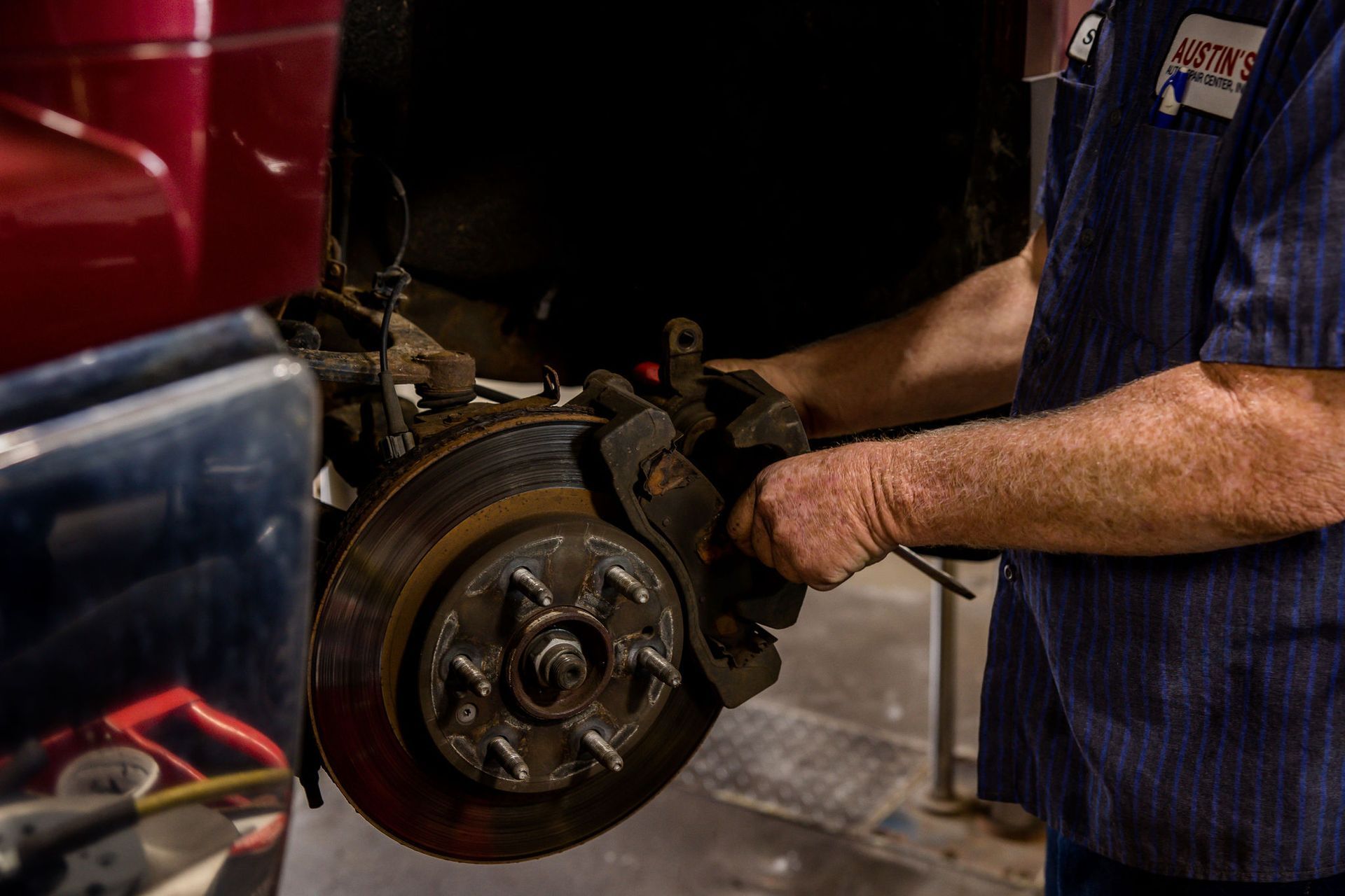 Mechanic working on a car's brake disc and caliper. Hands holding tools, garage setting.