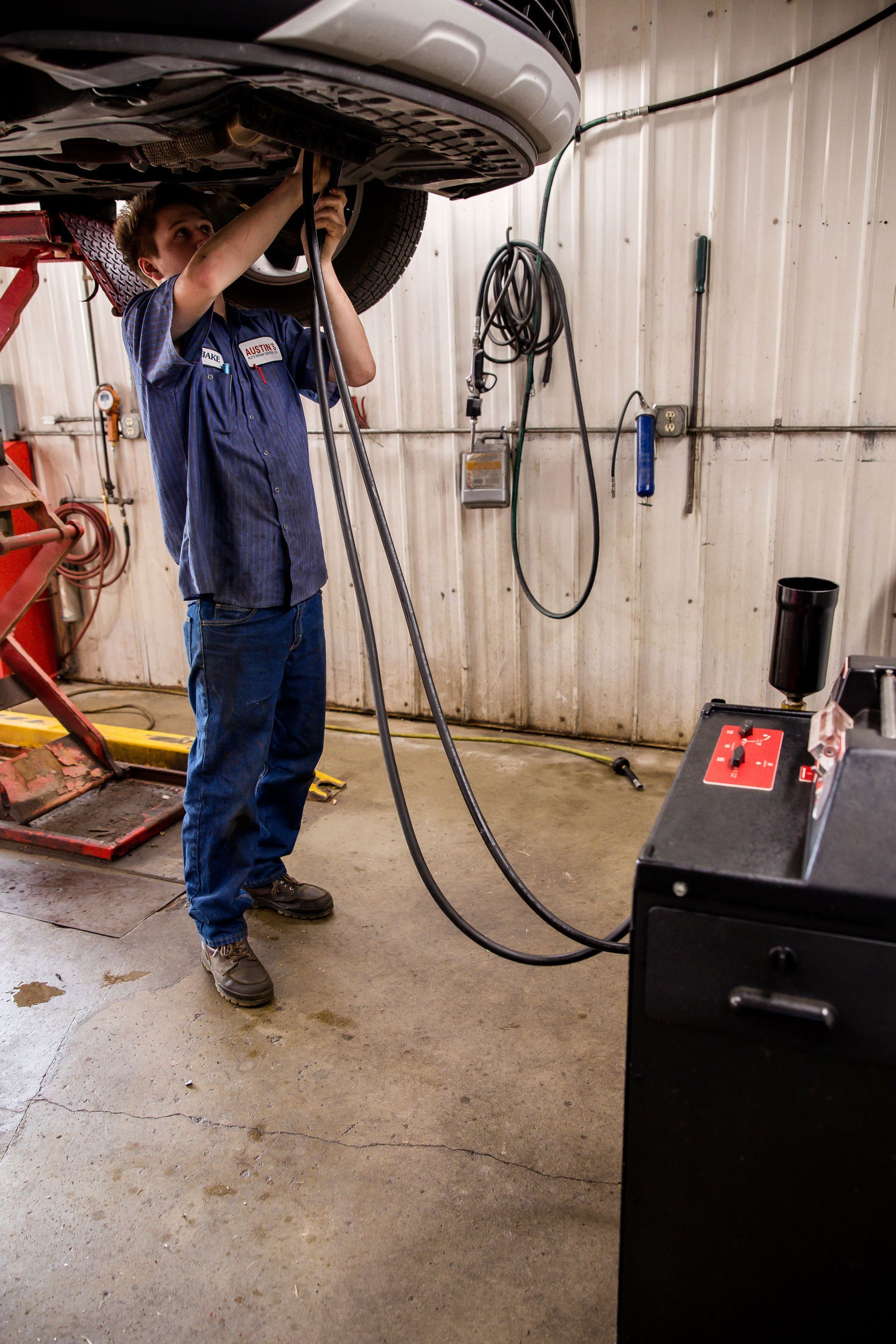 Mechanic under a car, connected to an oil changing machine in a garage.