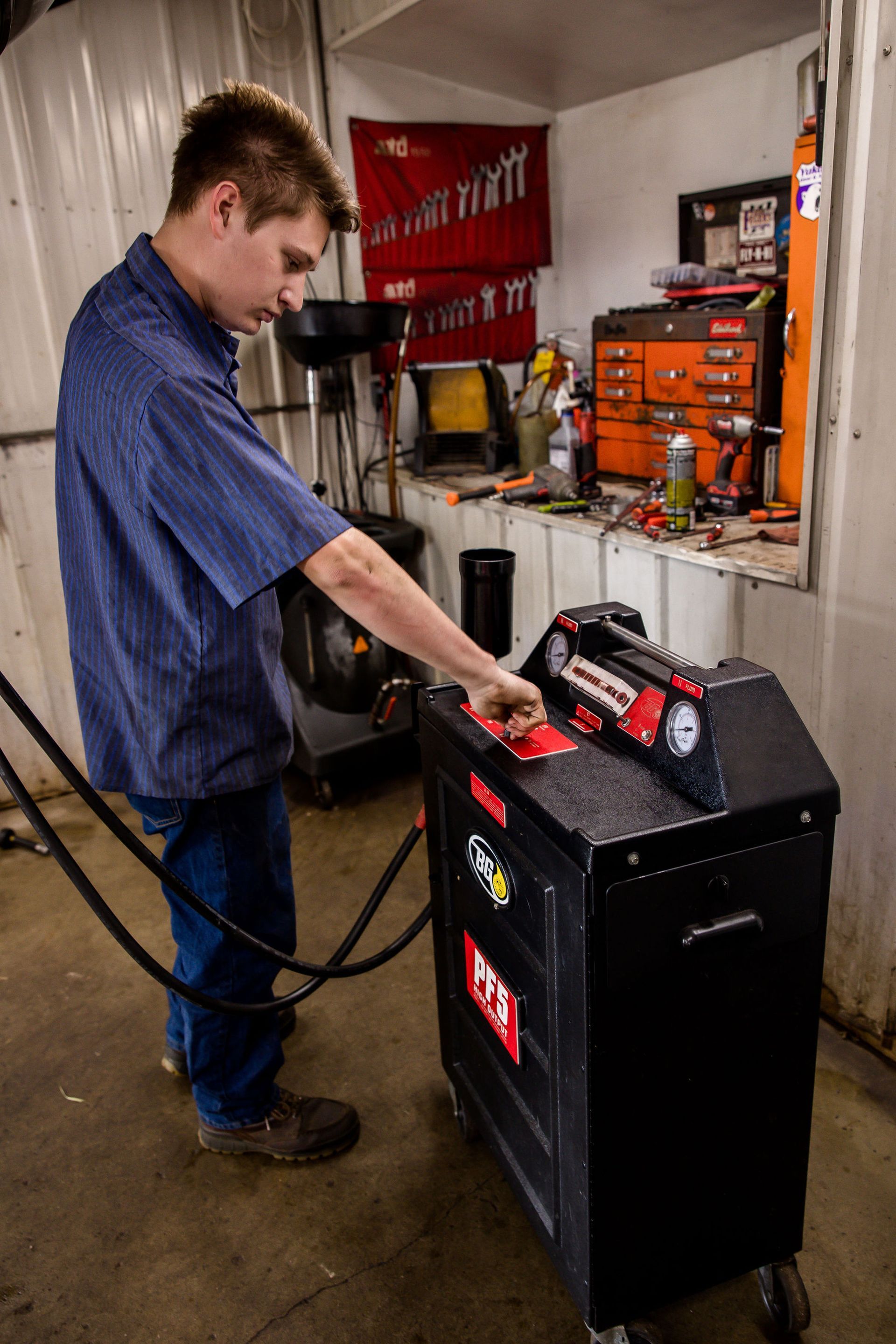 Mechanic in blue shirt working on a black machine, likely in a garage.