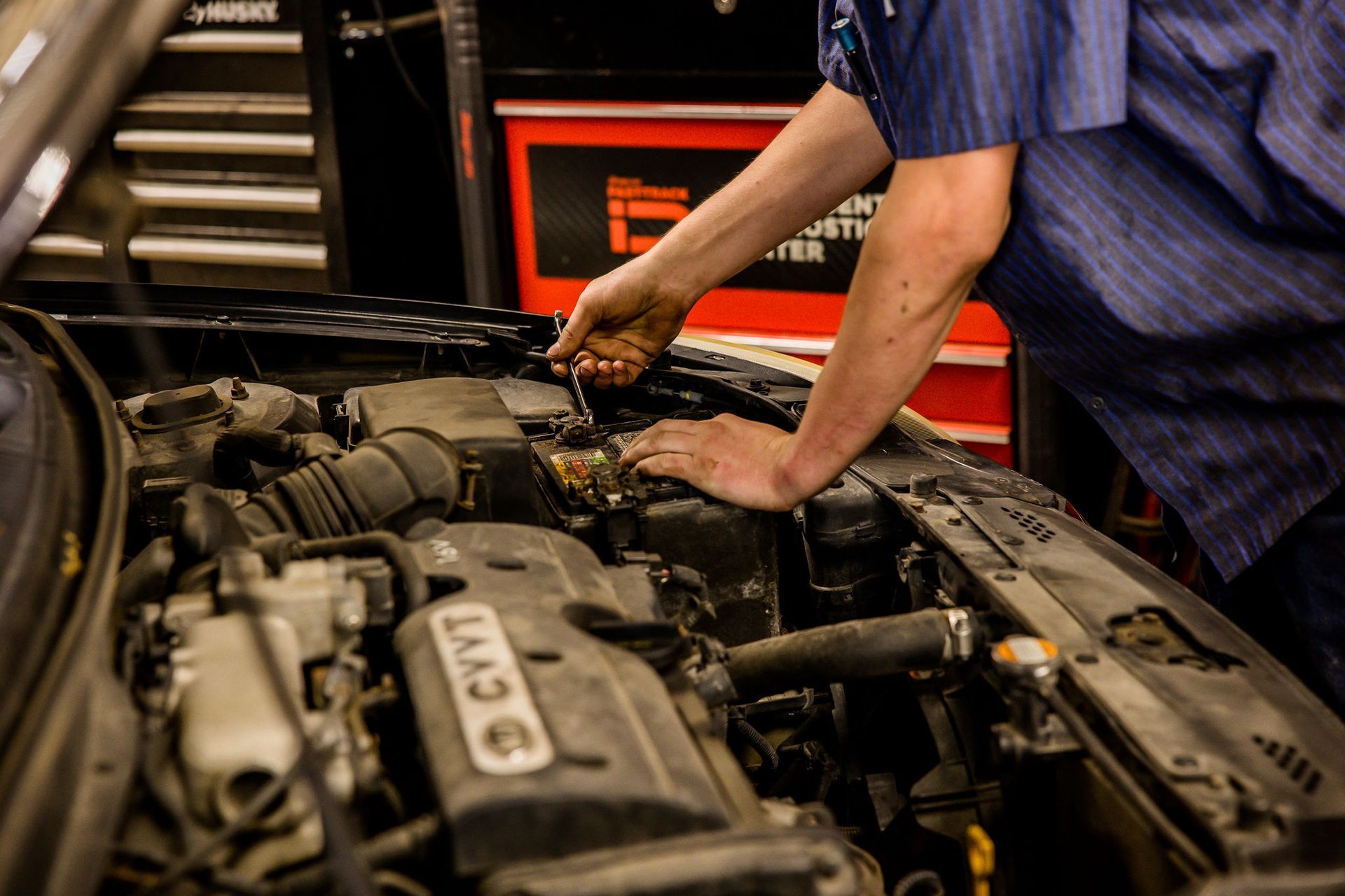 Mechanic working on a car engine with tools; shop setting.