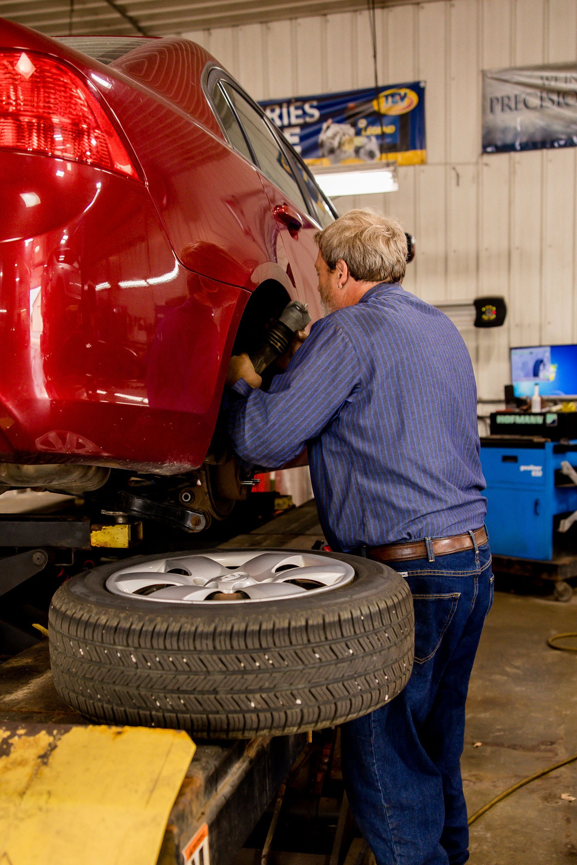 Mechanic working on the wheel of a red car in a repair shop. A spare tire rests below.