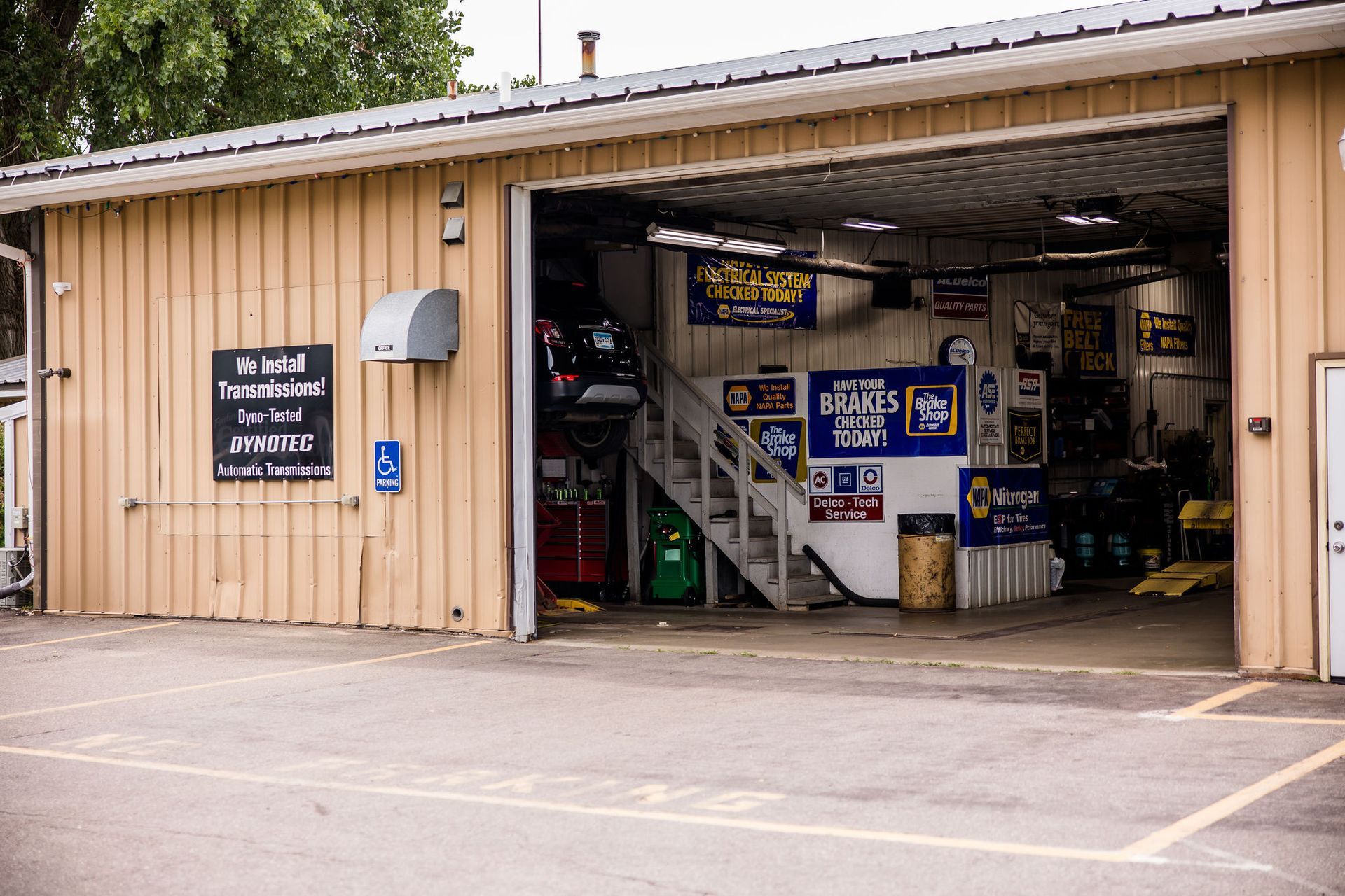 Garage exterior with open bay door; tan building, signs, and equipment visible inside.