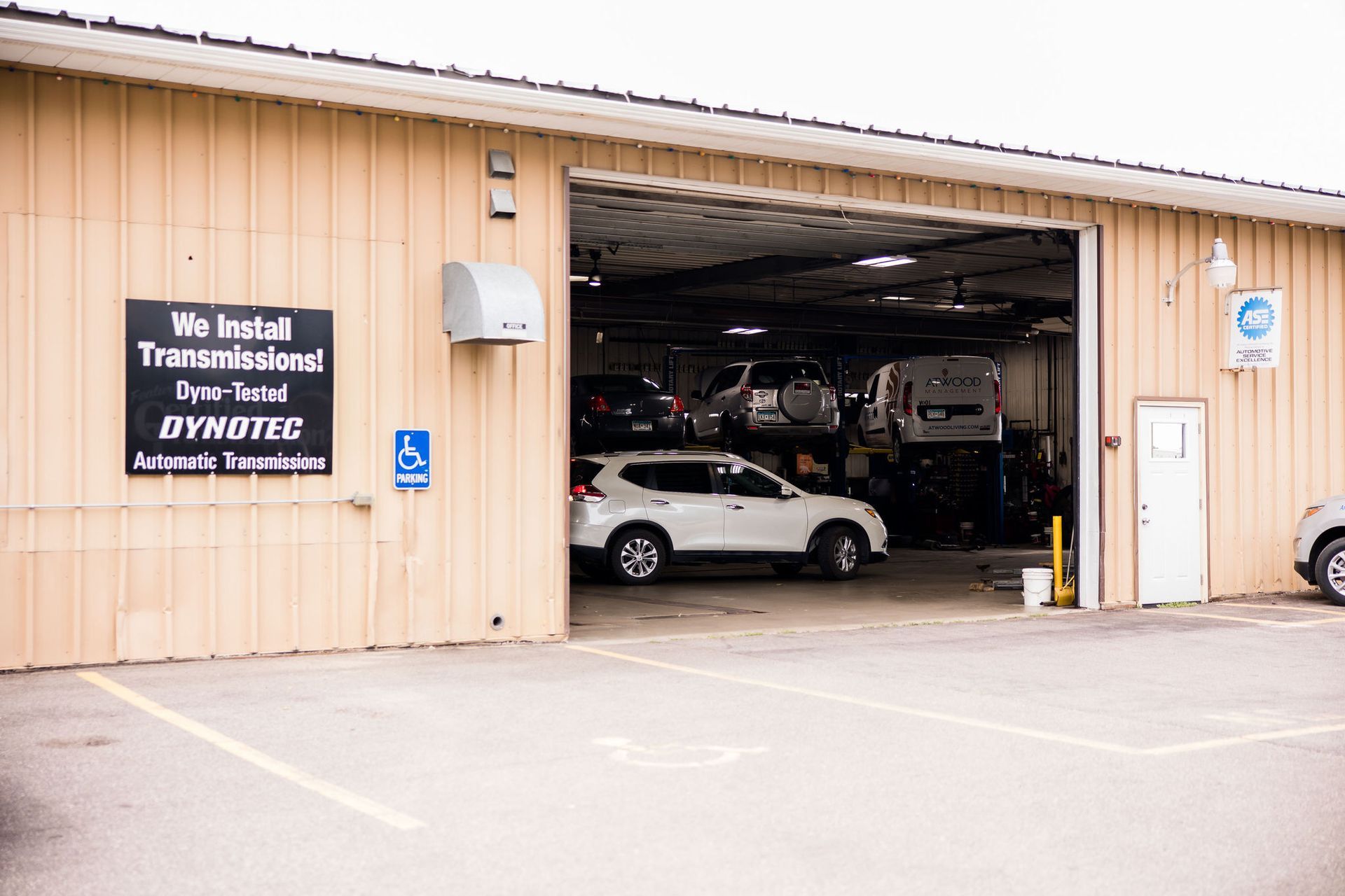 Exterior of a car repair shop with several vehicles inside, a white SUV is parked in front.
