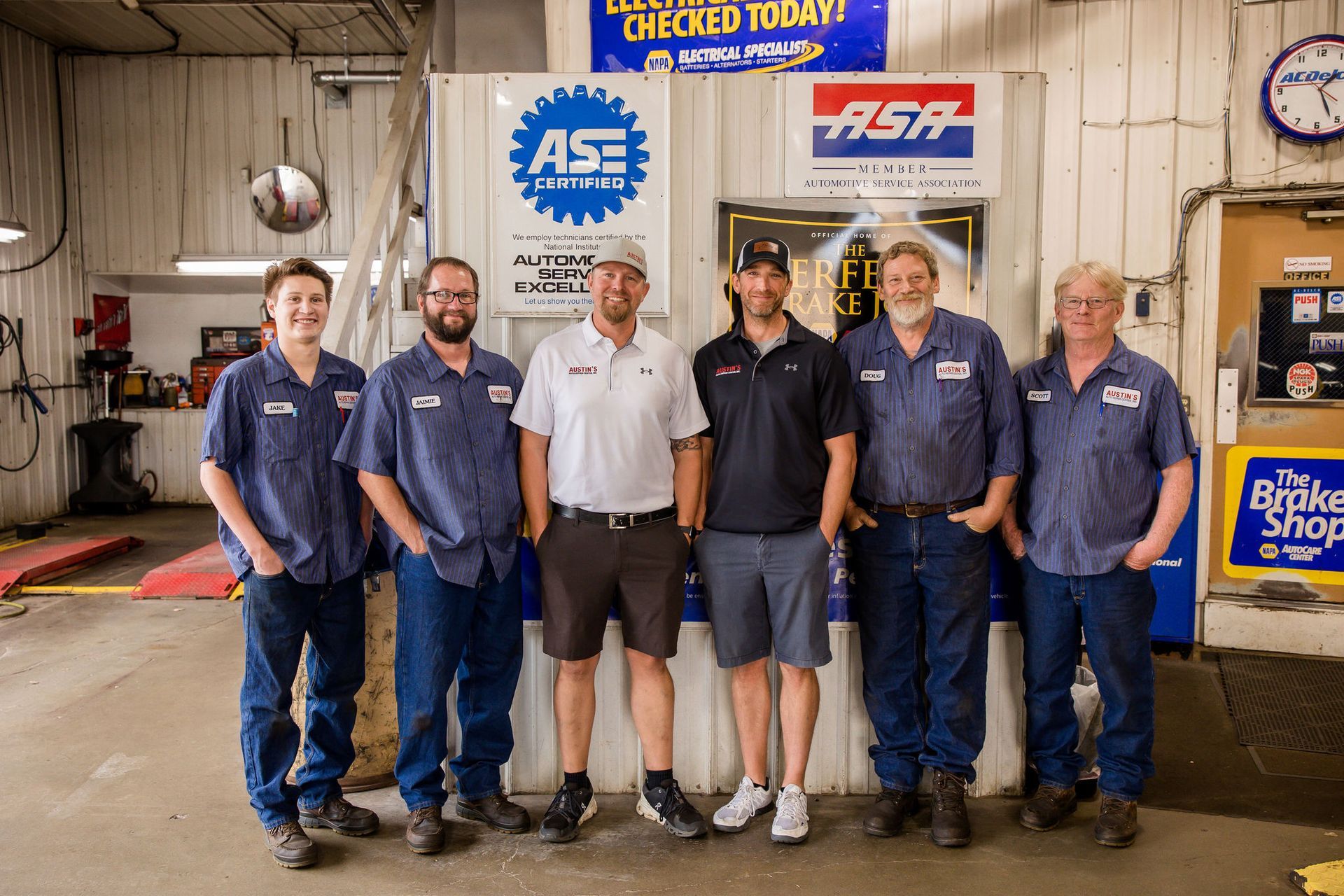 Six mechanics in a garage, smiling, posing in front of ASE and ASA signs.