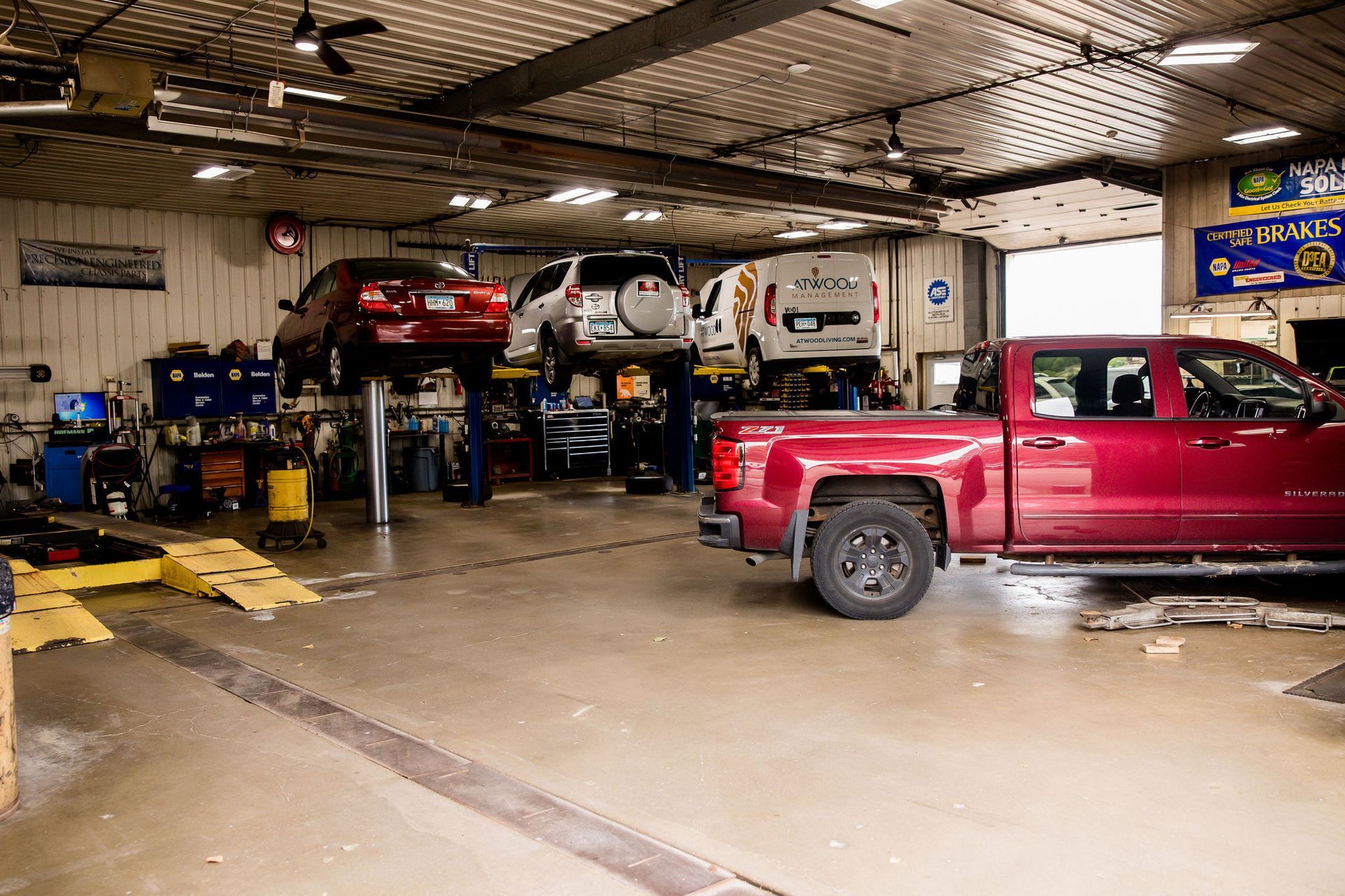 Interior of an auto repair shop with multiple cars on lifts and a truck on the ground.