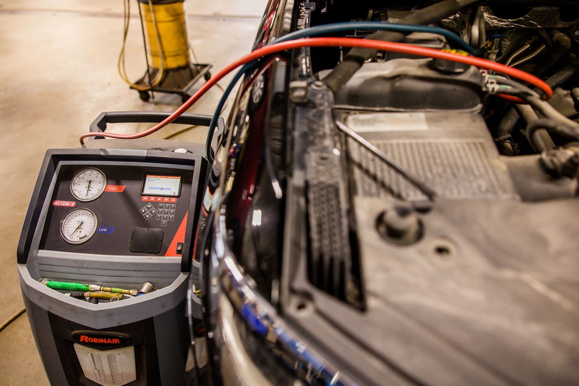 An auto shop with a machine connected to a car engine. Hoses are attached, gauges visible.