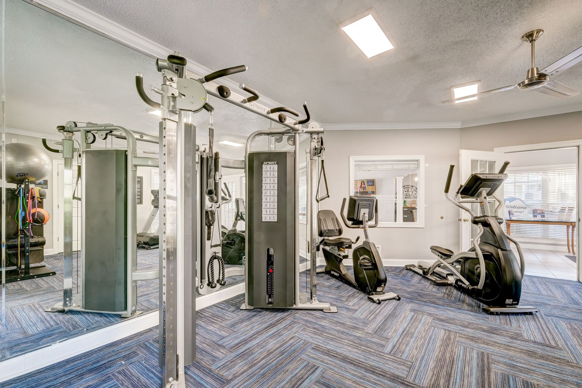 A residential gym featuring a cable weight machine, an exercise bike, an elliptical, and a large wall mirror.