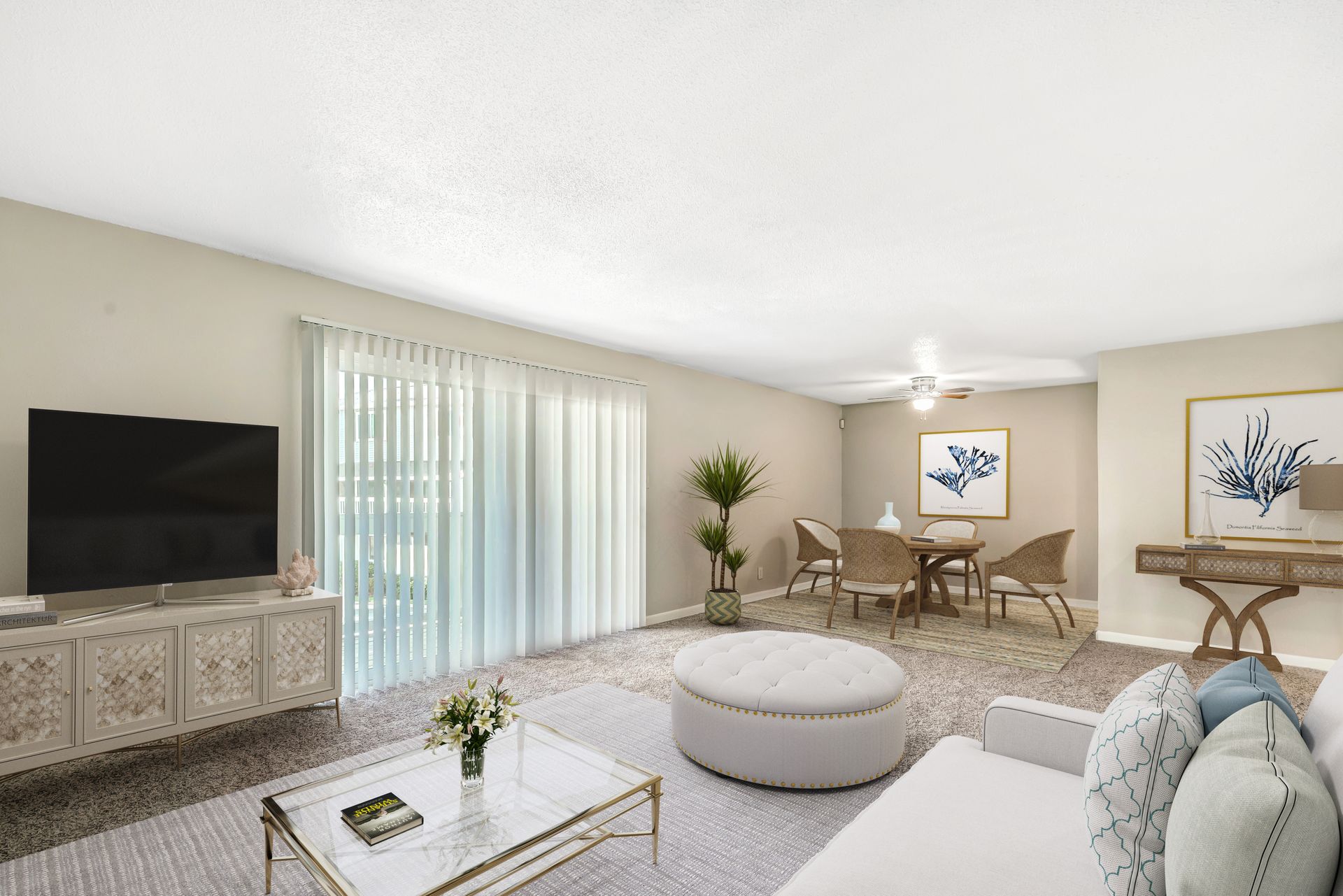 A spacious living and dining room with light neutral walls, a white sofa, a round ottoman, and a wooden dining set.