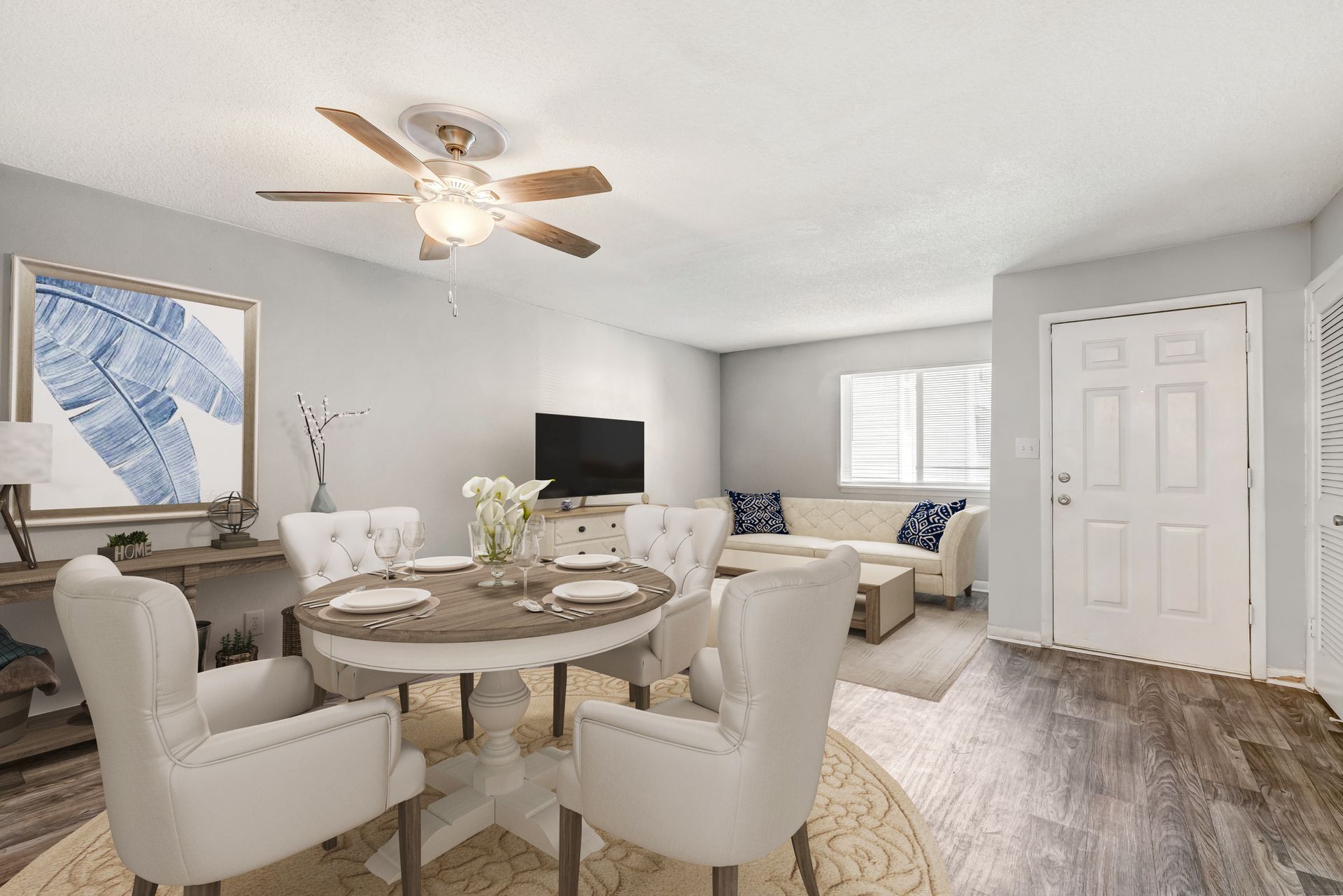 A dining room with a round wooden table and white tufted chairs, leading into a living area with a sofa and TV.