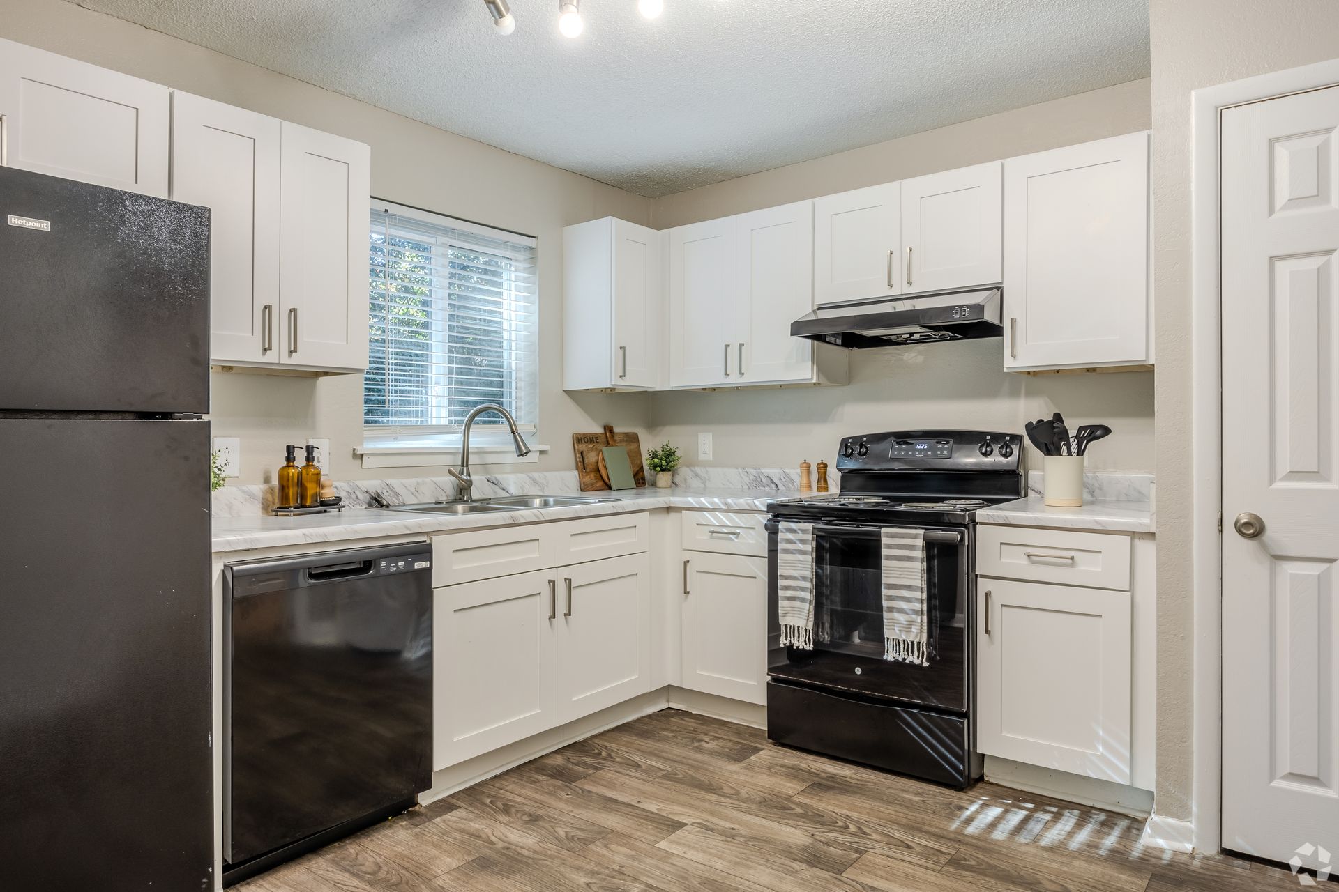 A bright, modern kitchen featuring white cabinets, stainless steel hardware, a black refrigerator, and wood-look flooring.