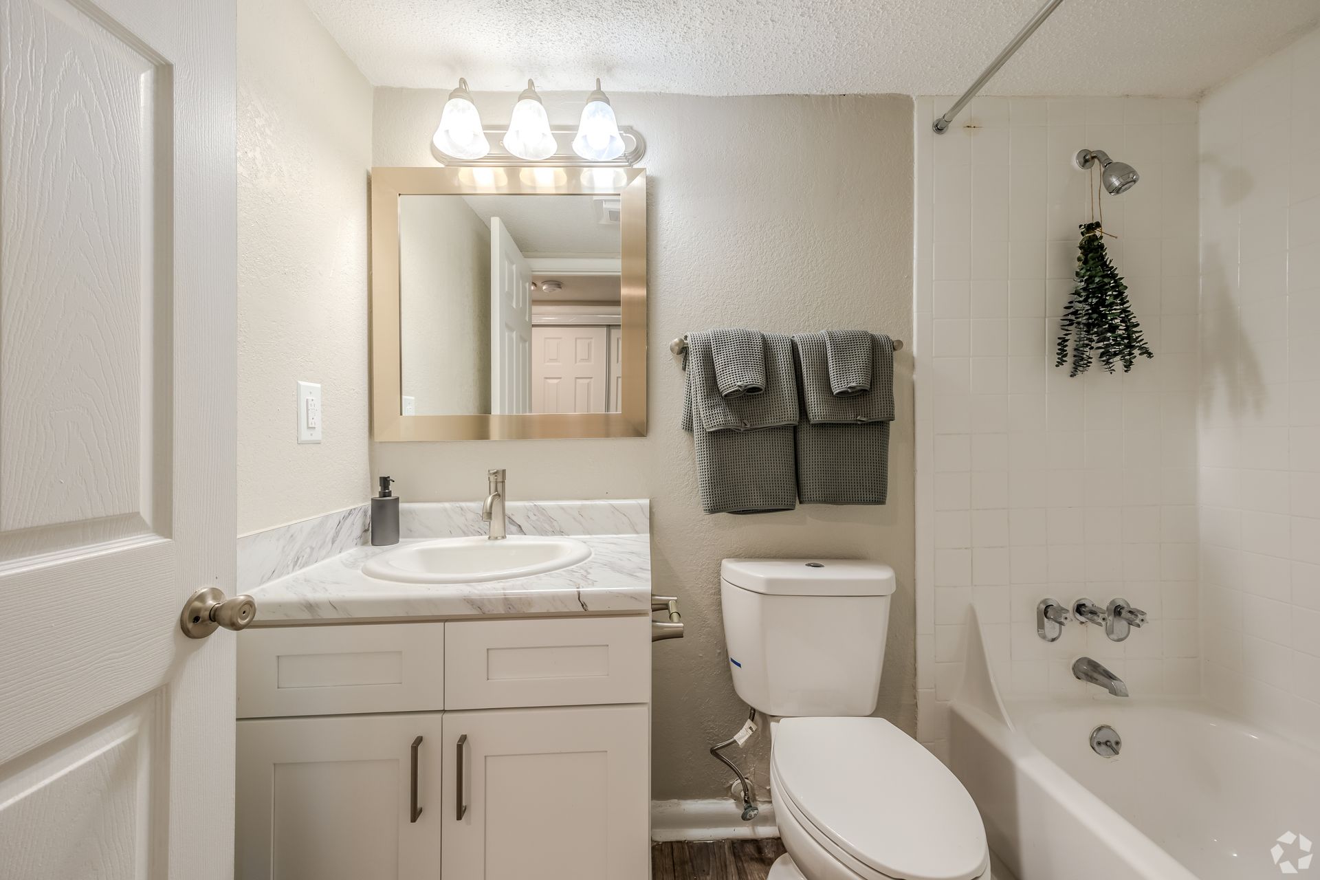 A small bathroom with a white vanity, marble countertop, toilet, and a bathtub with a shower head and gray towels.
