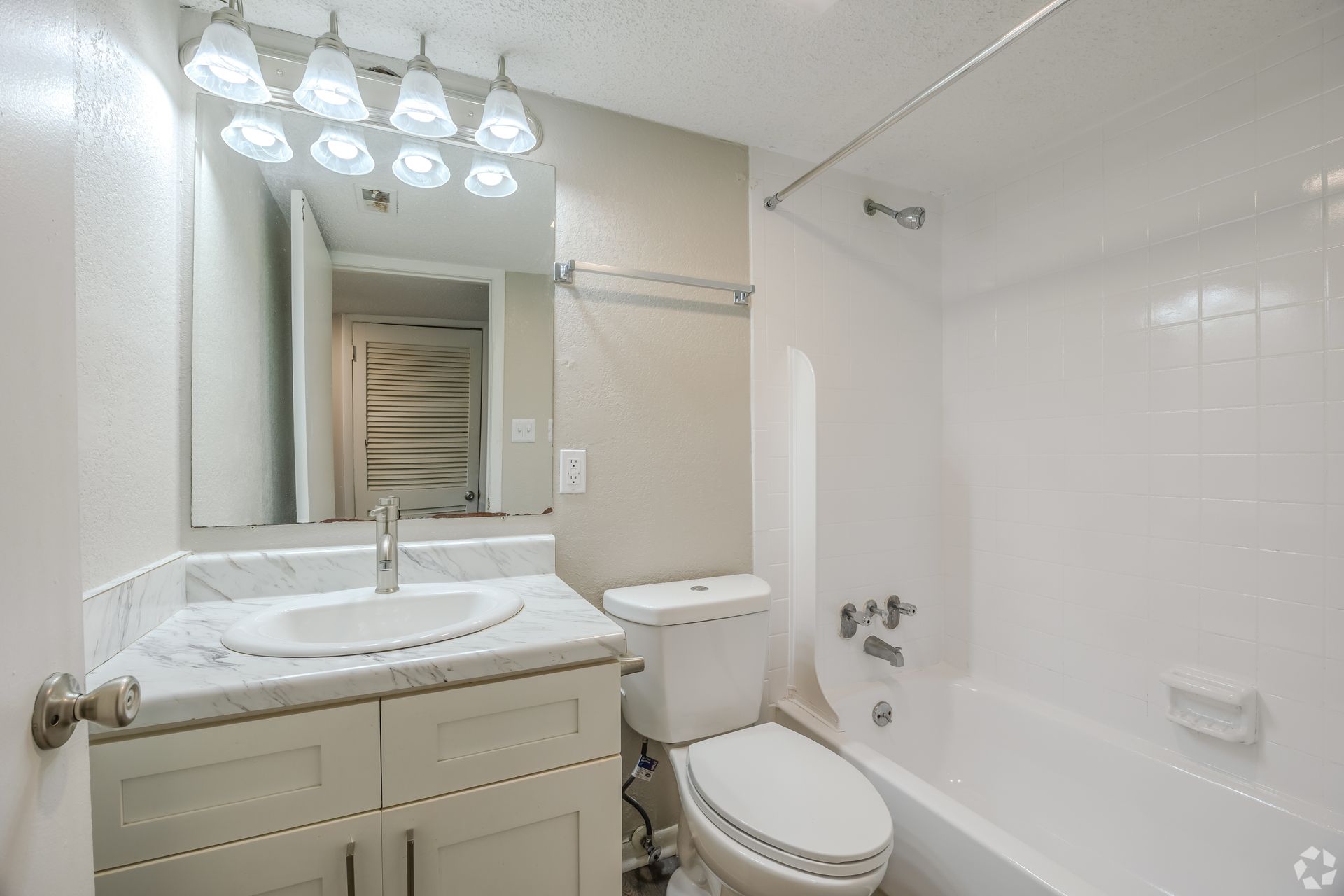 A modern bathroom with a white marble-topped vanity, a wall mirror, a toilet, and a bathtub with a shower head.