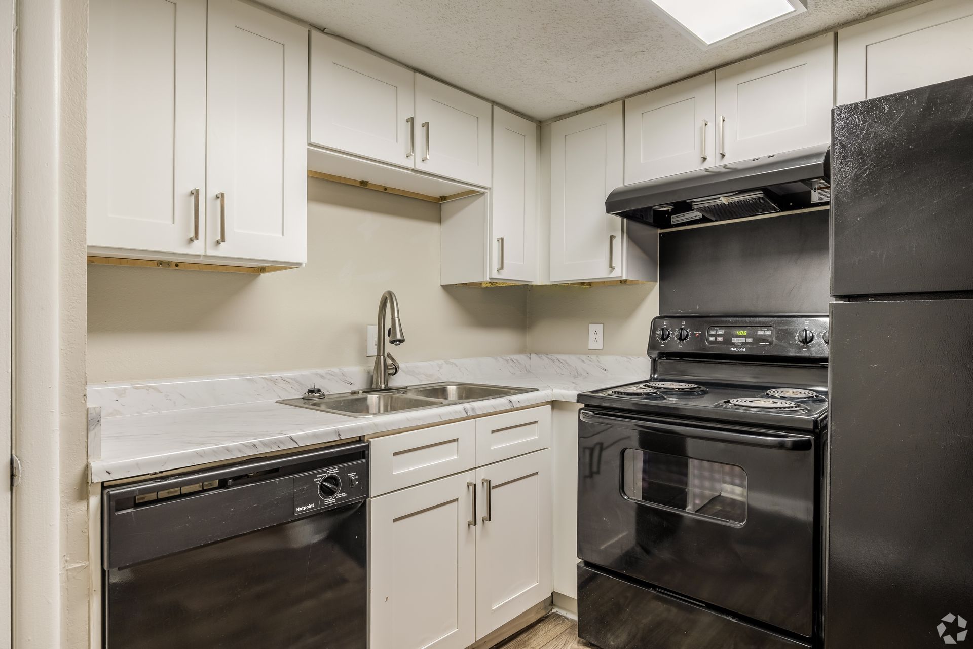 Small kitchen with white cabinets, marble-patterned countertops, and black appliances including a stove and dishwasher.