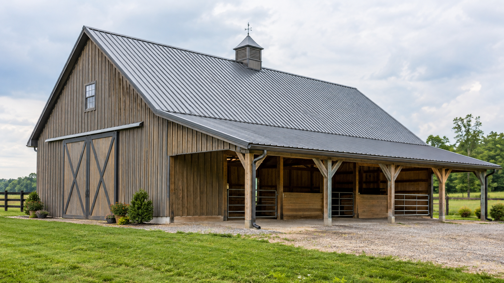 Rustic barn with a gray metal roof and open front on a grassy farm under cloudy skies