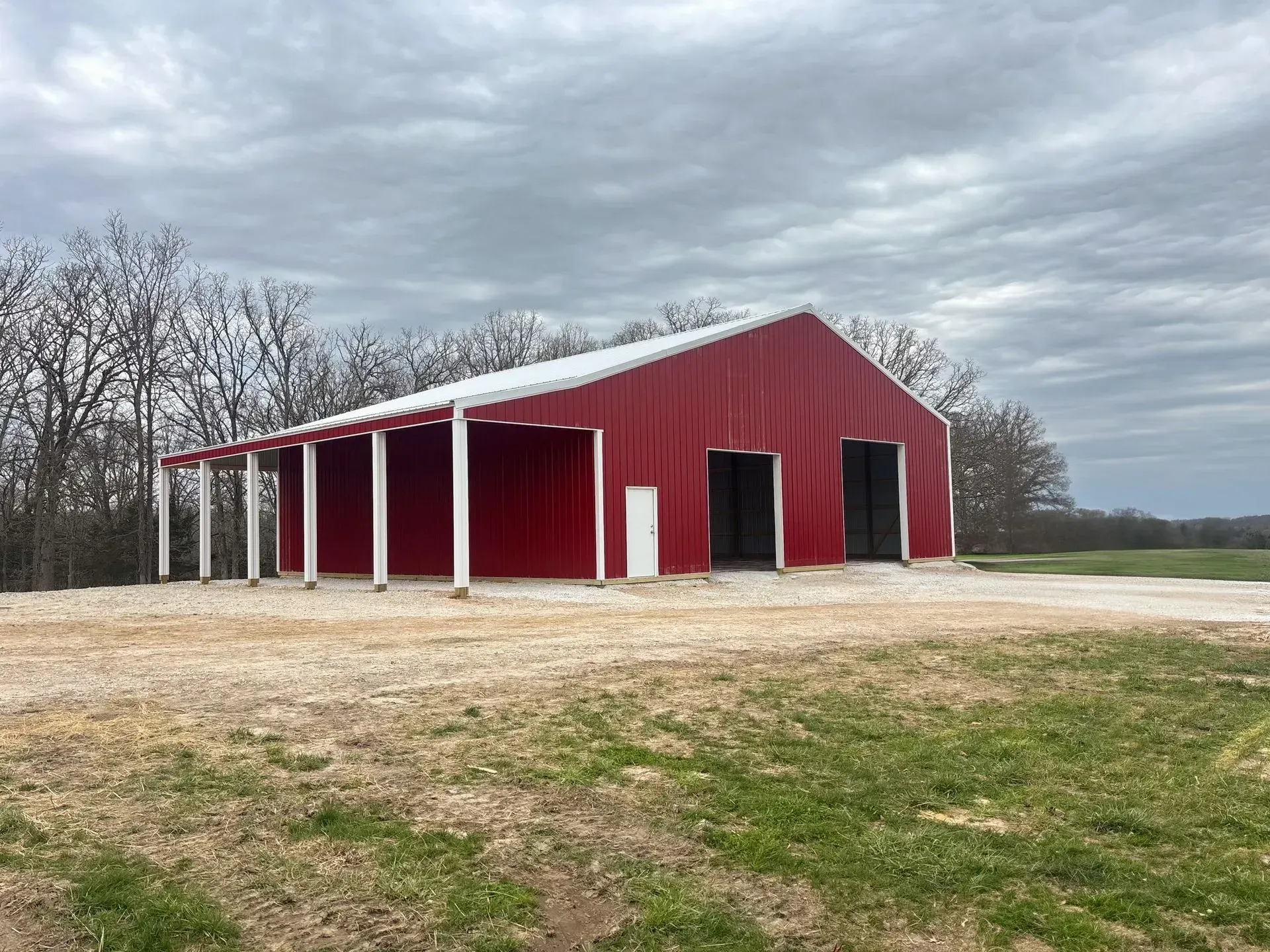 Red barn with white trim on a rural grassy lot under a cloudy sky
