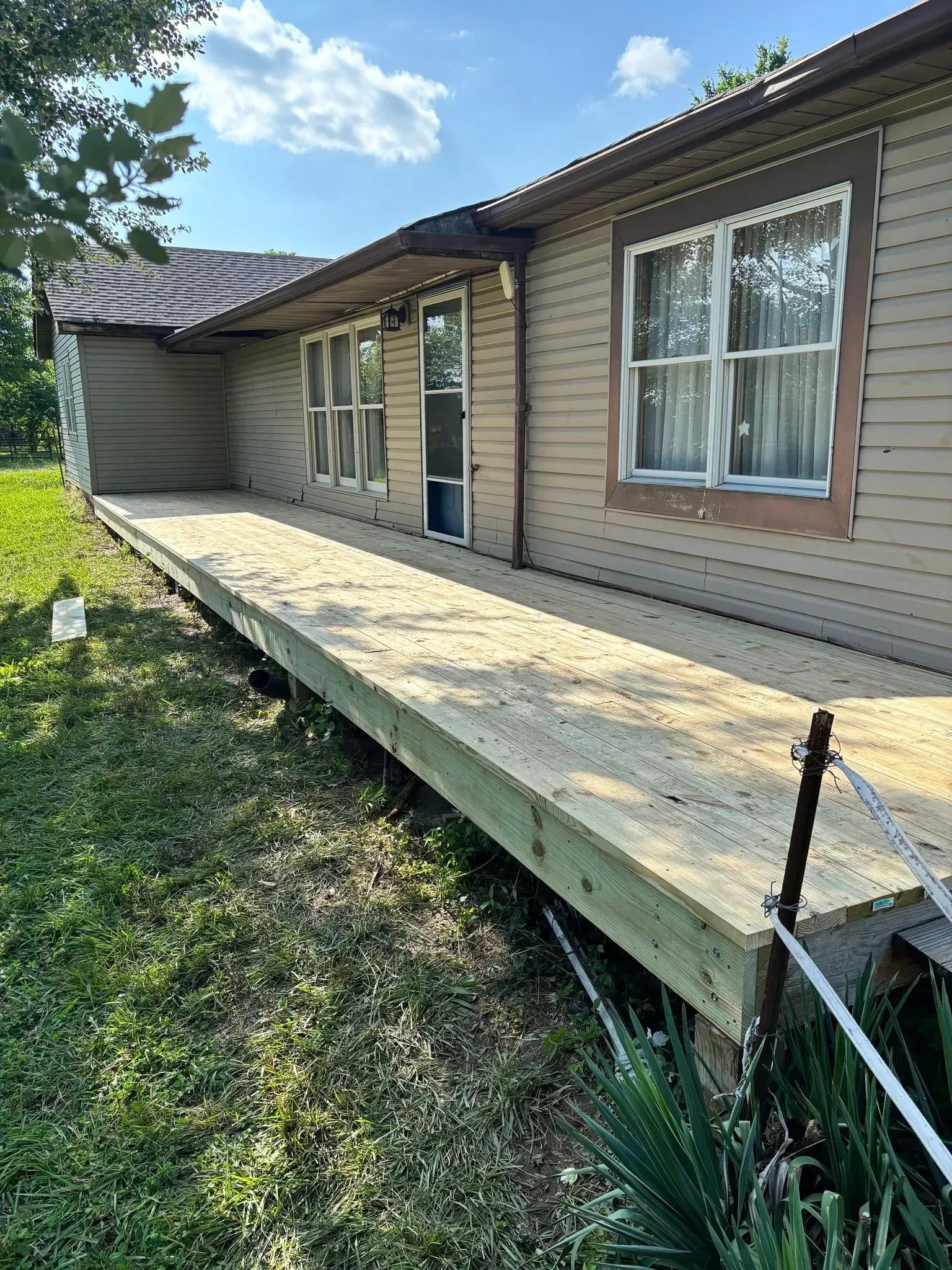Wooden accessibility ramp leading to a house entrance beside beige siding and brown-trimmed windows.