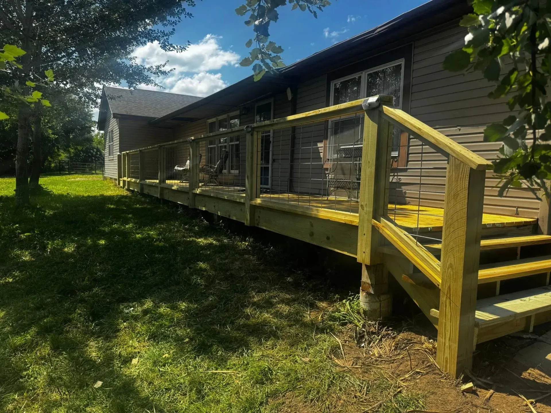 Yellow wooden ramp and stairs leading to a brown building on a sunny grassy property.
