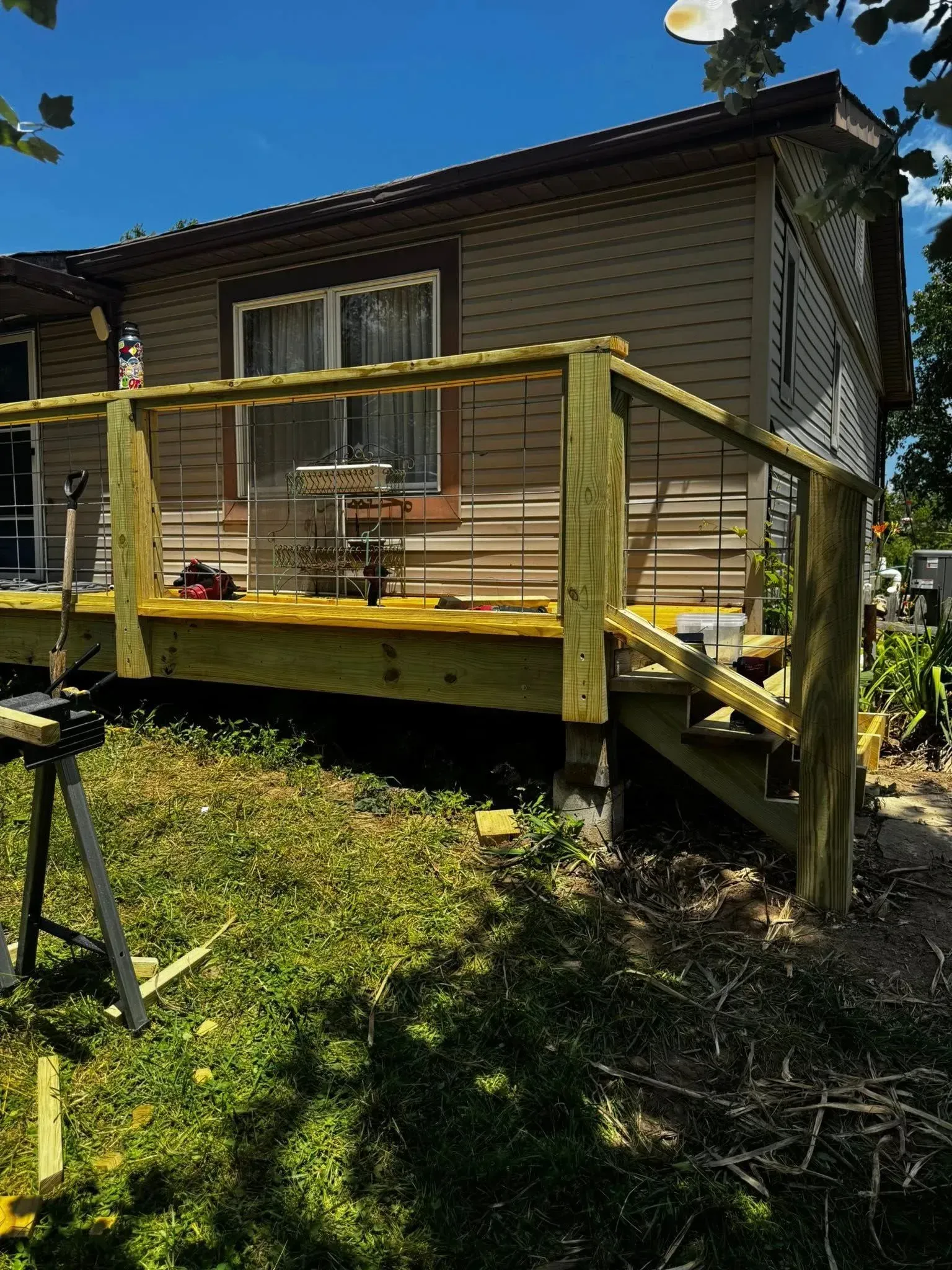 Yellow wooden deck attached to a house on a grassy slope under a blue sky