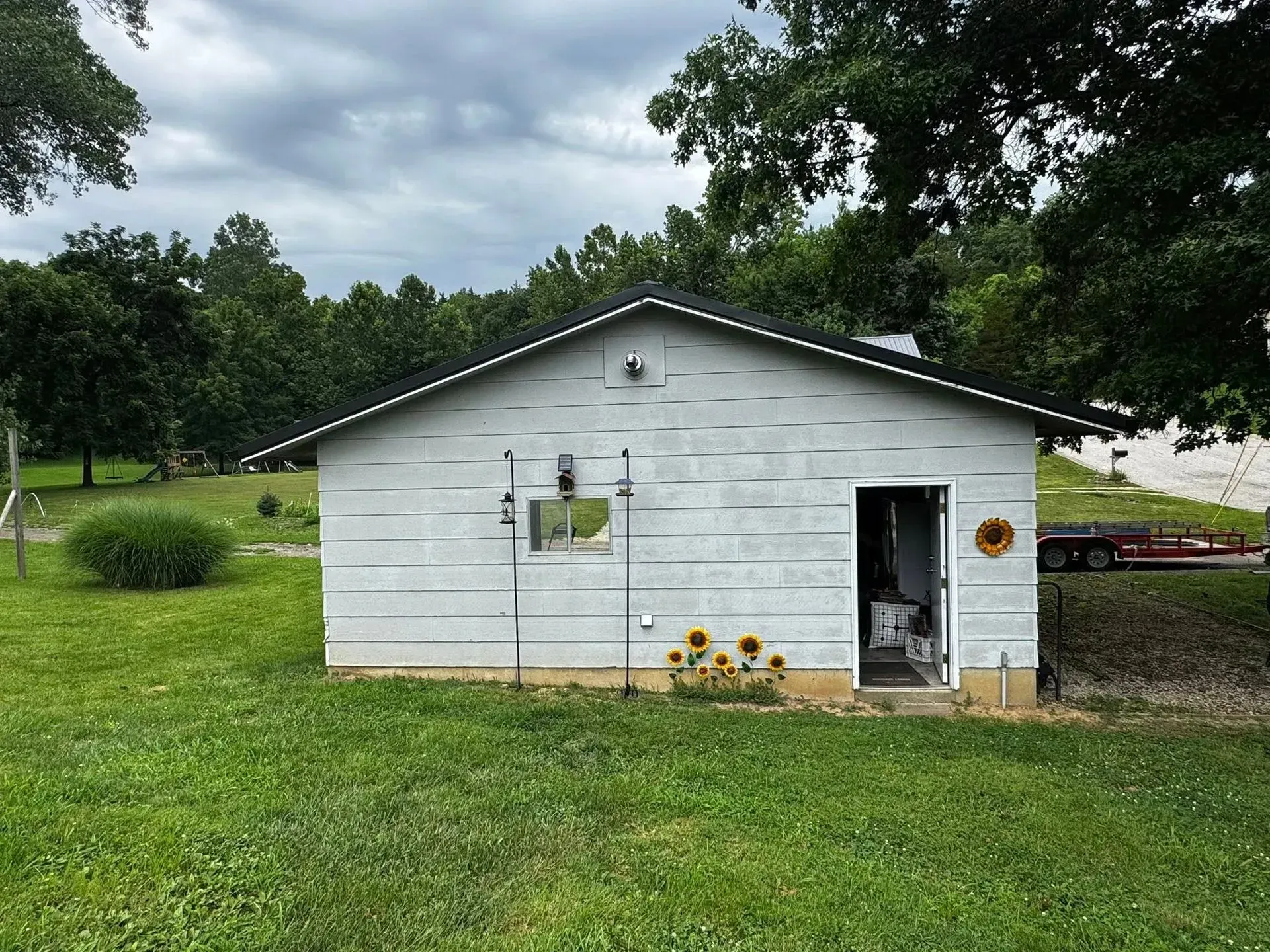 Small white shed with open door in a grassy yard, with trees and cloudy sky behind it