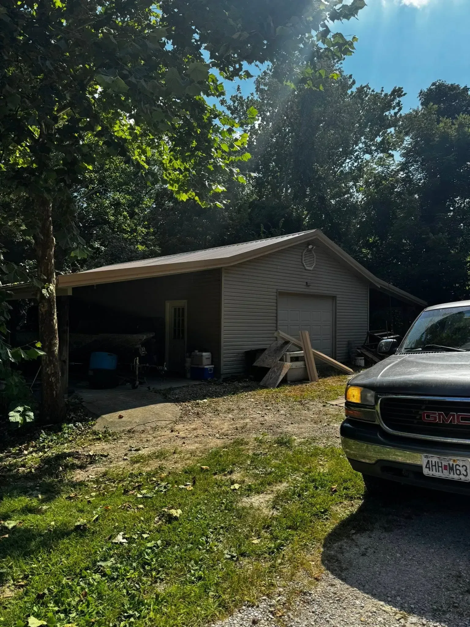 Wooded driveway with a small garage and a parked black car in bright sunlight