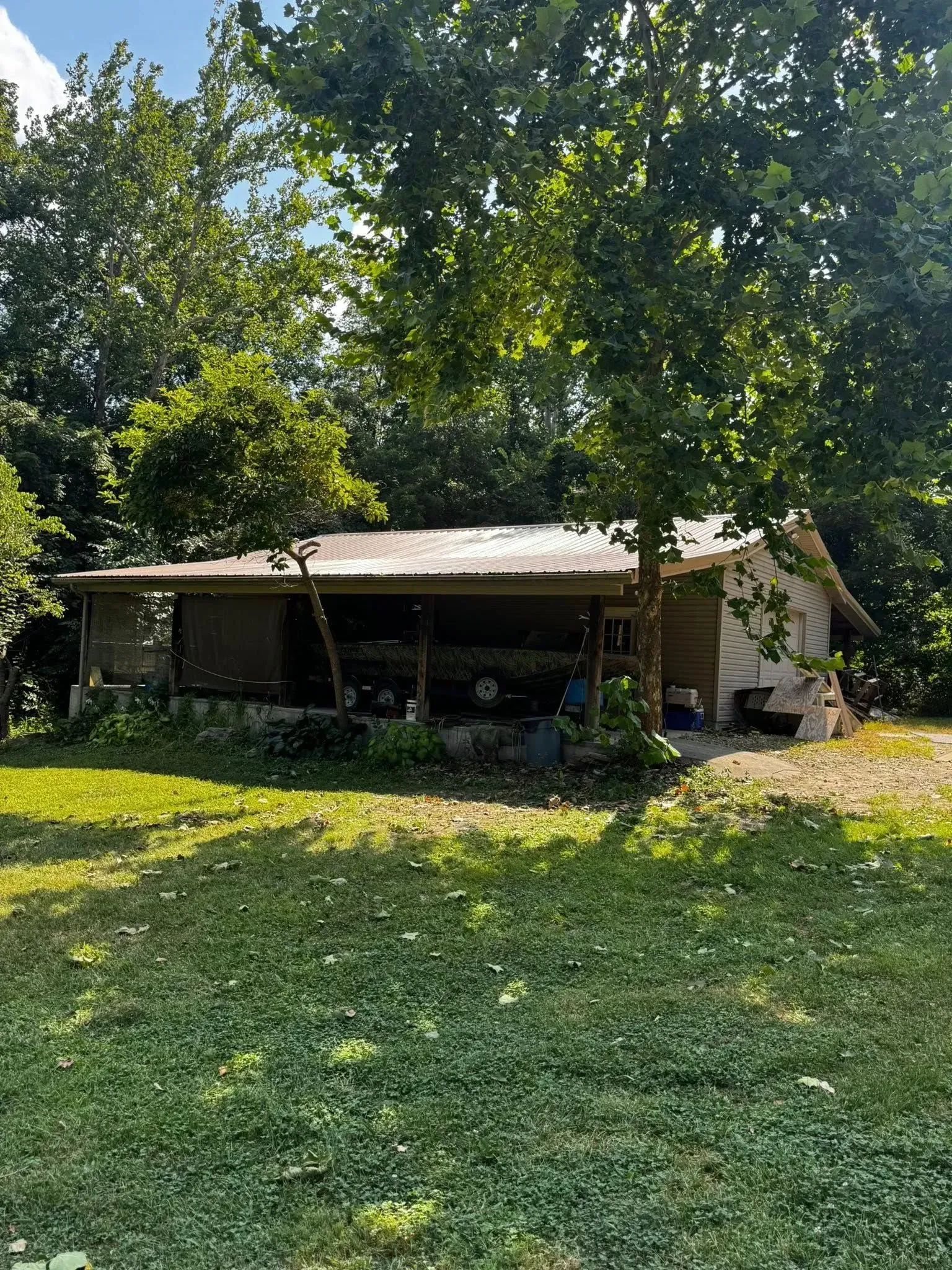 Small rustic cabin with a metal roof in a grassy yard, surrounded by trees in bright daylight