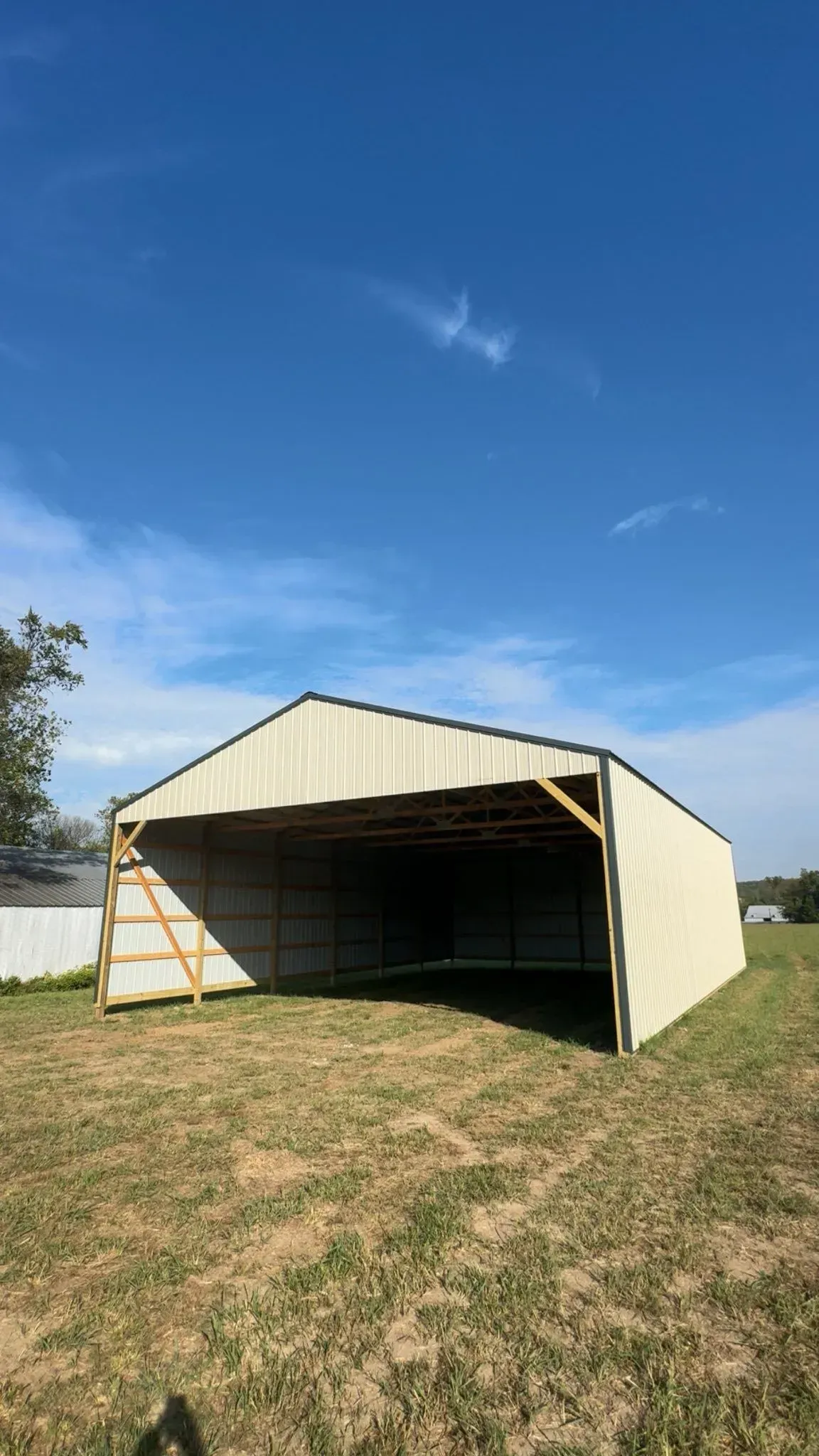 Open metal shed with beige sides in a grassy yard under a clear blue sky