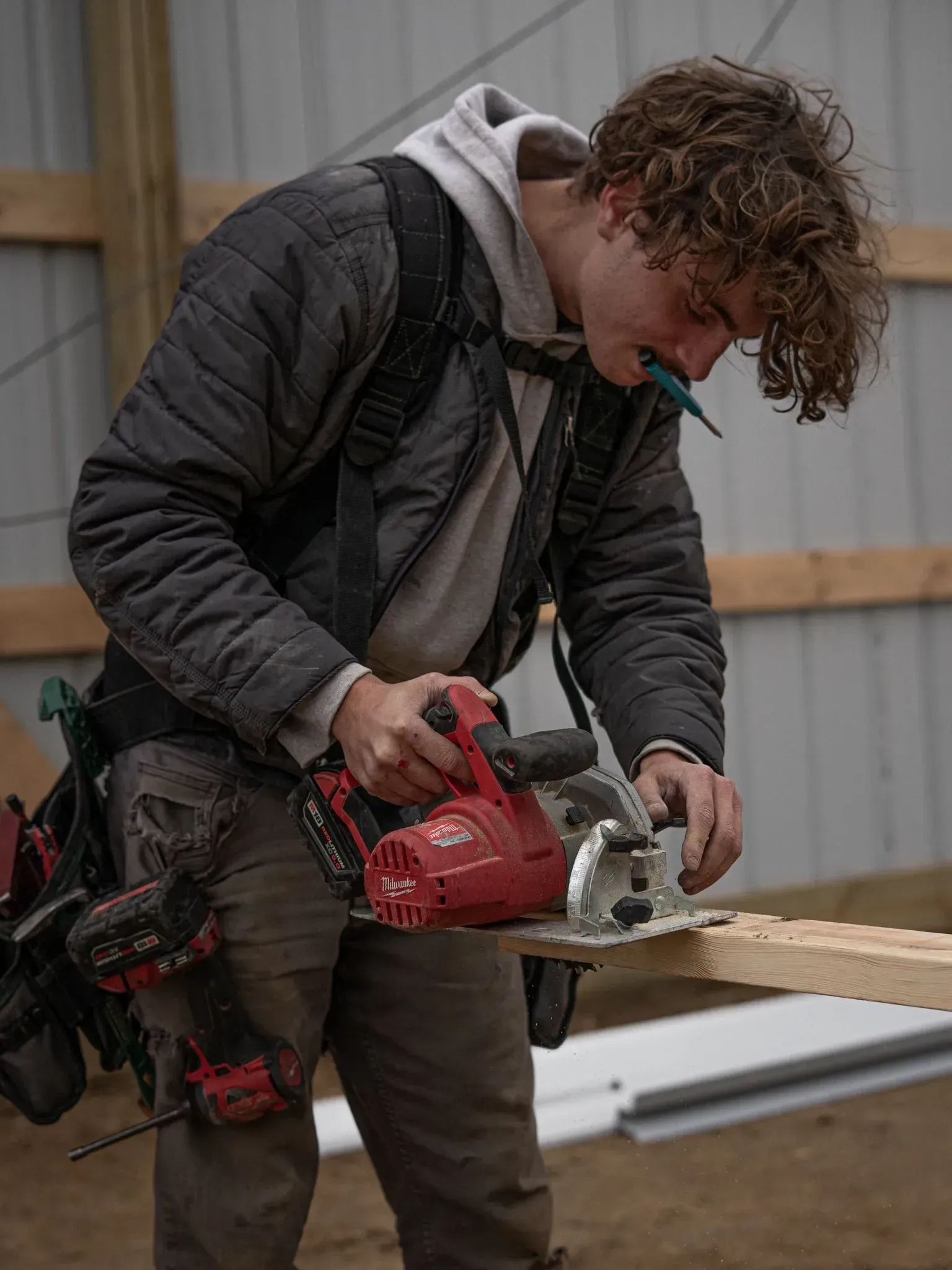 Person cutting a wooden plank with a red chainsaw outdoors near a building