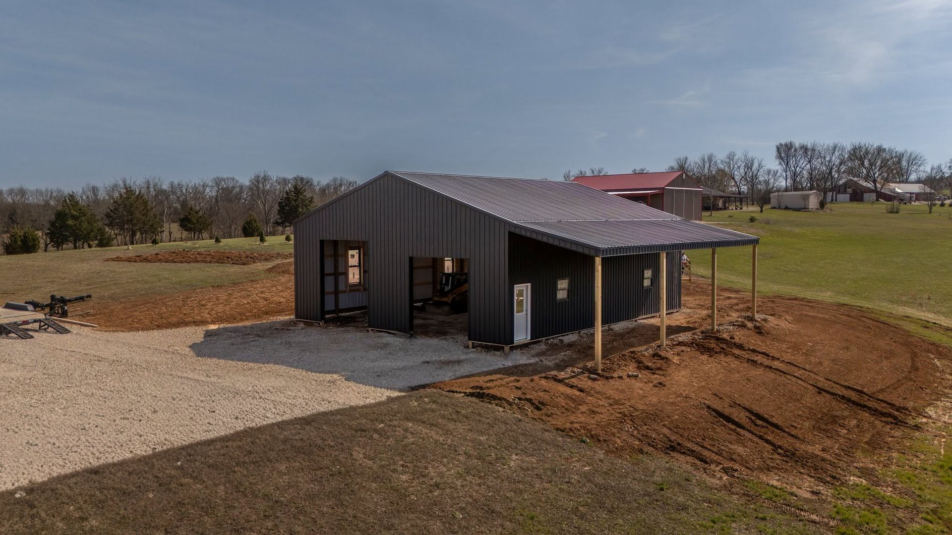 Small dark-gray house on a gravel lot in a rural field under a clear sky