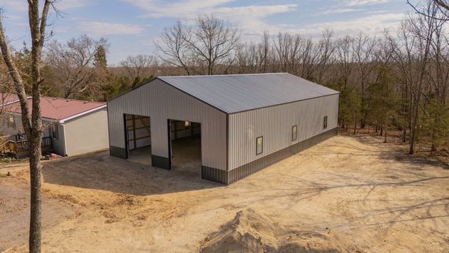 Metal-sided barn on a dirt lot, with open doors and trees in the background.