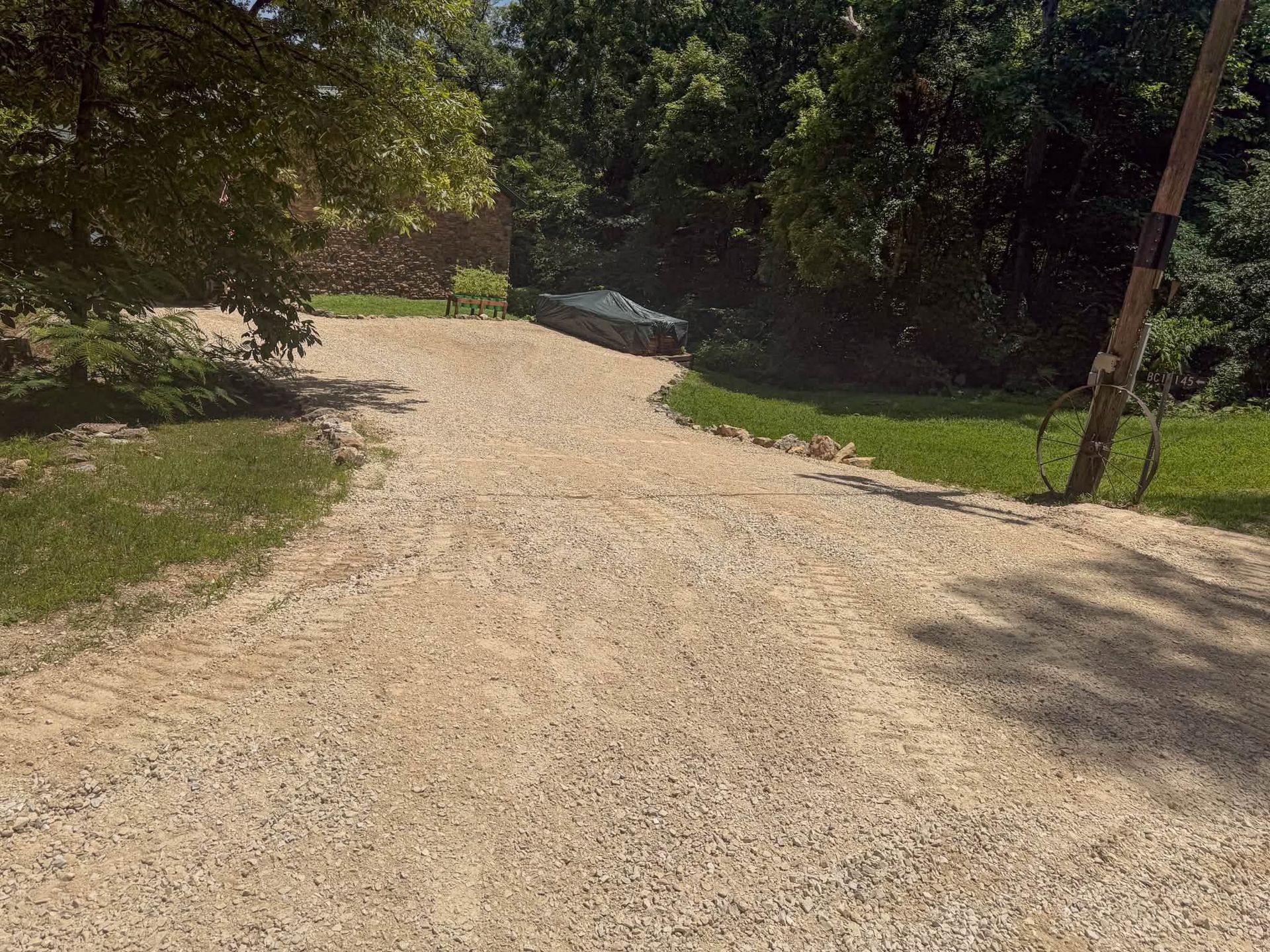 Gravel driveway curving through a shaded green yard toward trees and a house in the distance