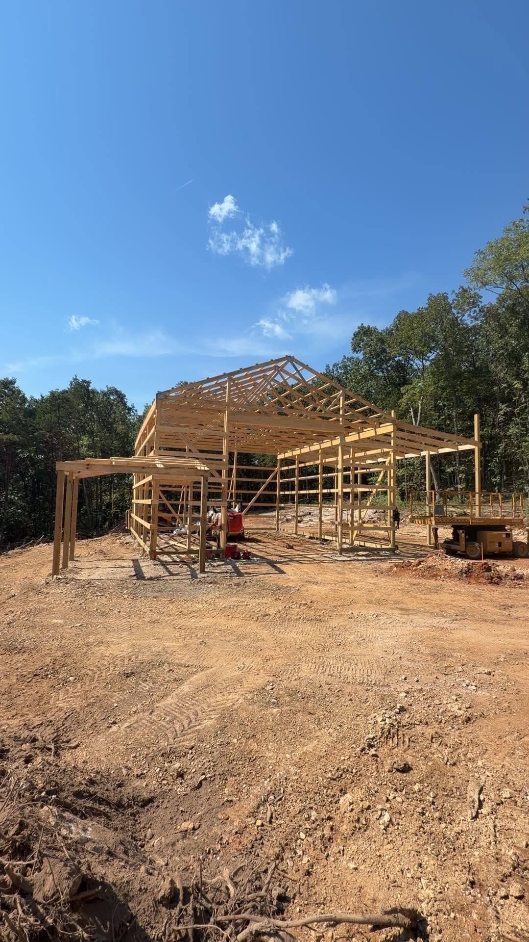 Wooden house frame under construction on a dirt lot beneath a clear blue sky
