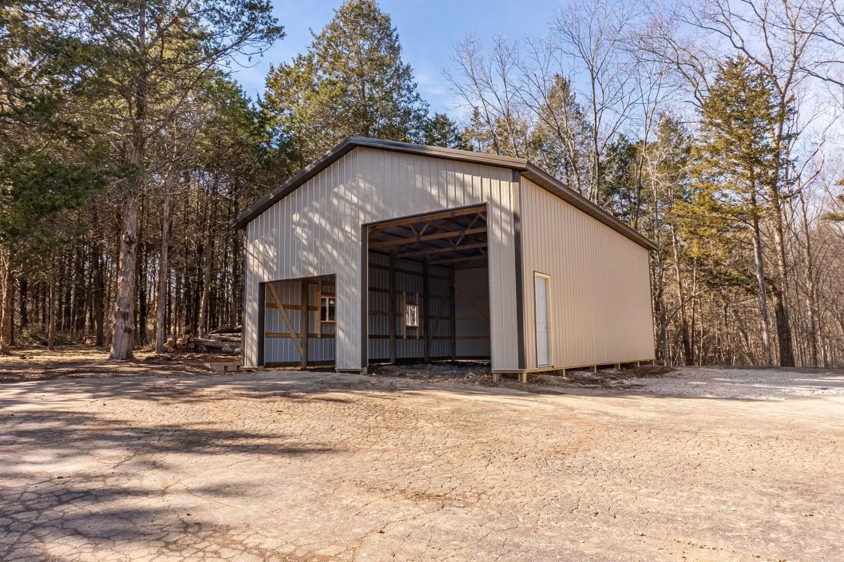 Large gray metal storage building with several open bays on a gravel lot under a clear blue sky