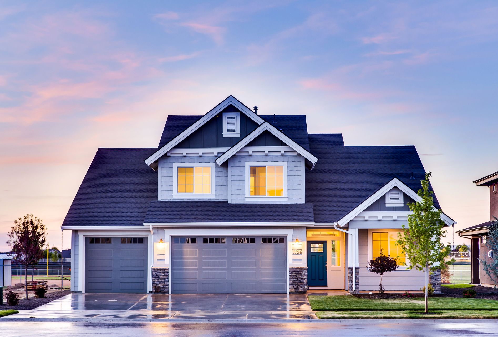 Modern gray two-story house with lit windows and garage at dusk
