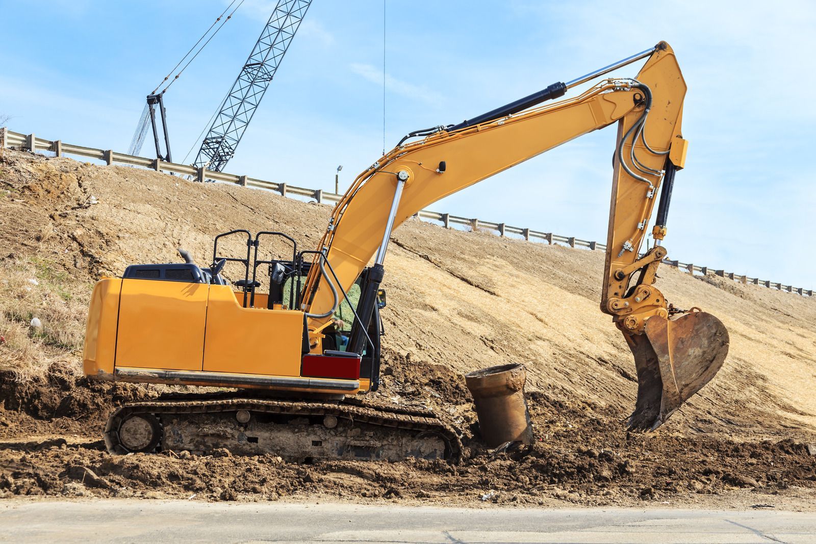 Yellow excavator digging dirt on a construction site beside a sloped earth bank