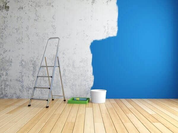 Una habitación vacía con una escalera y un cubo de pintura.