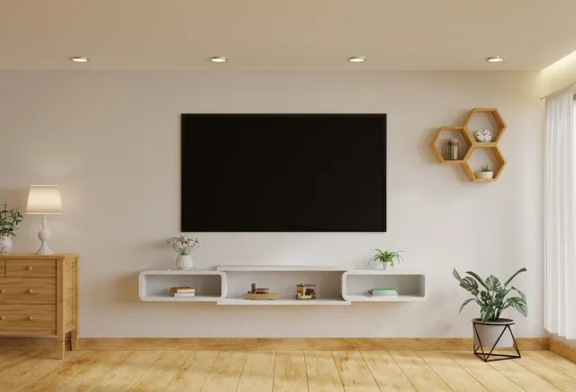 Living room with a large TV, floating shelf, wooden floor, and decorative plants.