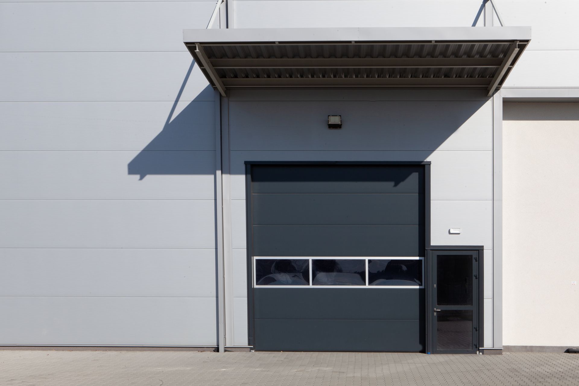 Gray industrial building with a large dark gray garage door, small door, and awning.