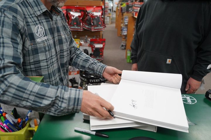Two people at a store counter looking through an open white notebook or sketchbook Two people at a store counter looking through an open white notebook or sketchbook