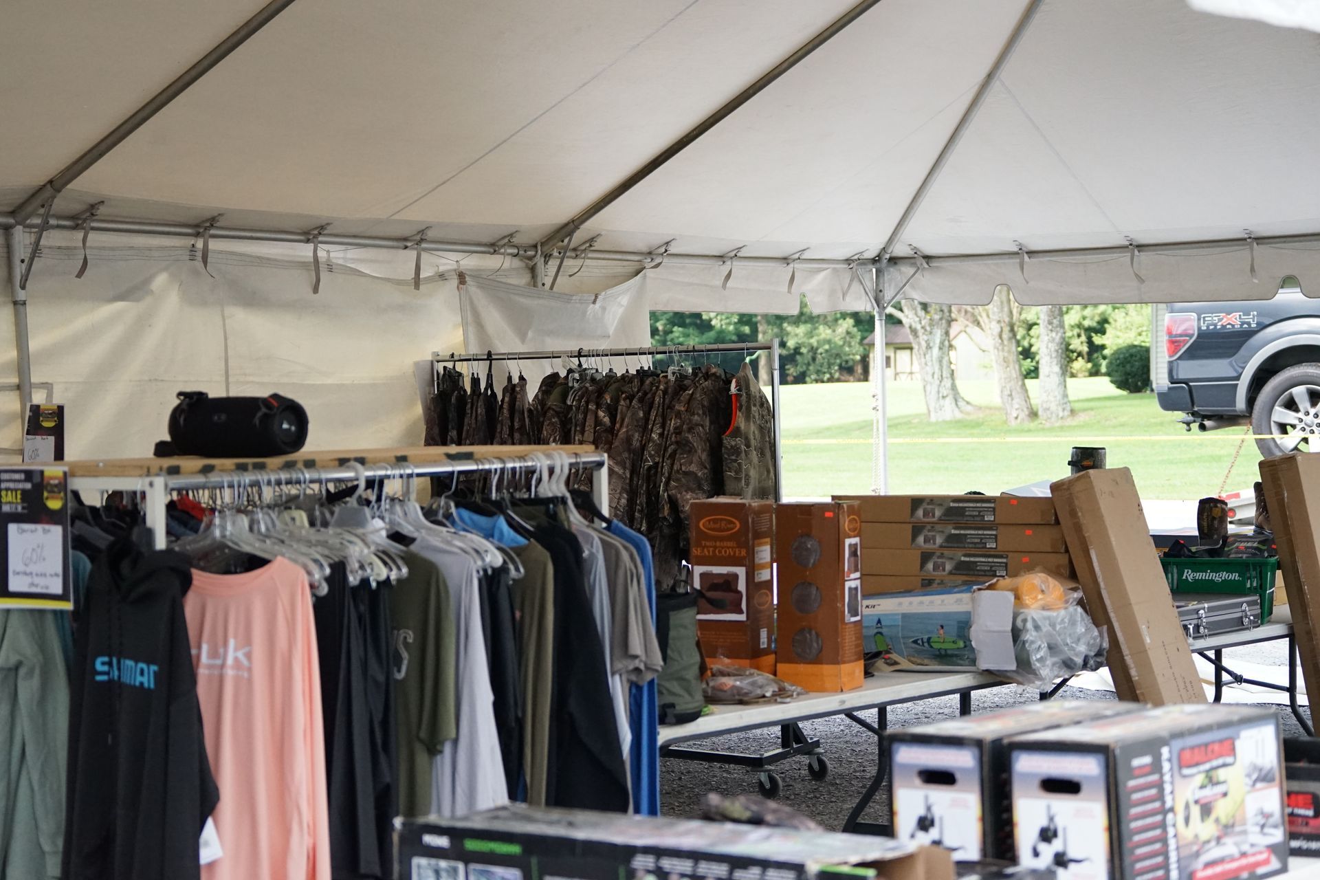 Outdoor market tent with clothing racks, boxes, and assorted merchandise displays.