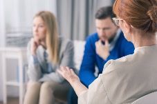 A woman is talking to a man and a woman in a therapy session.